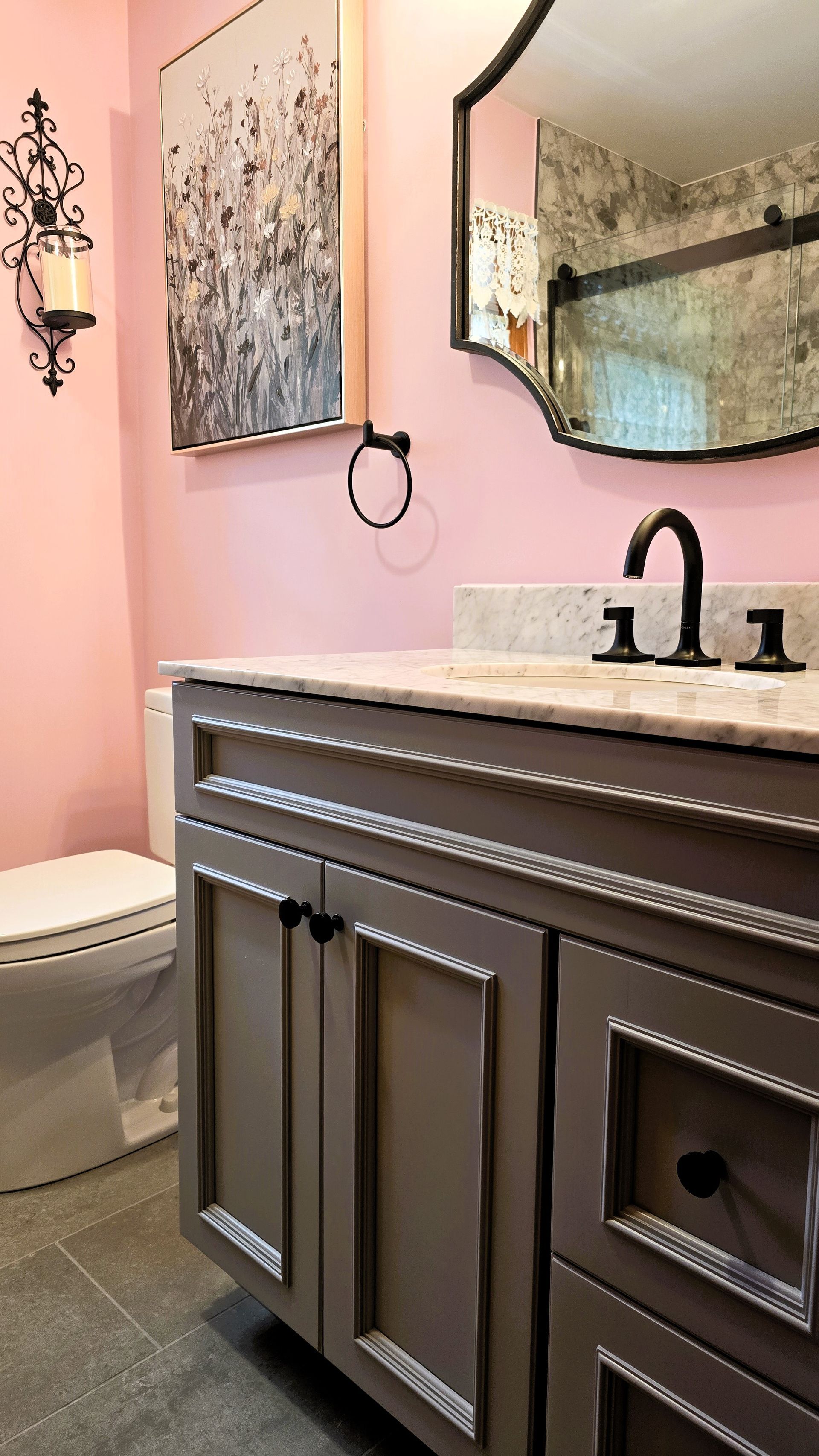 Pink bathroom with gray vanity, art, ornate mirror, and black fixtures.