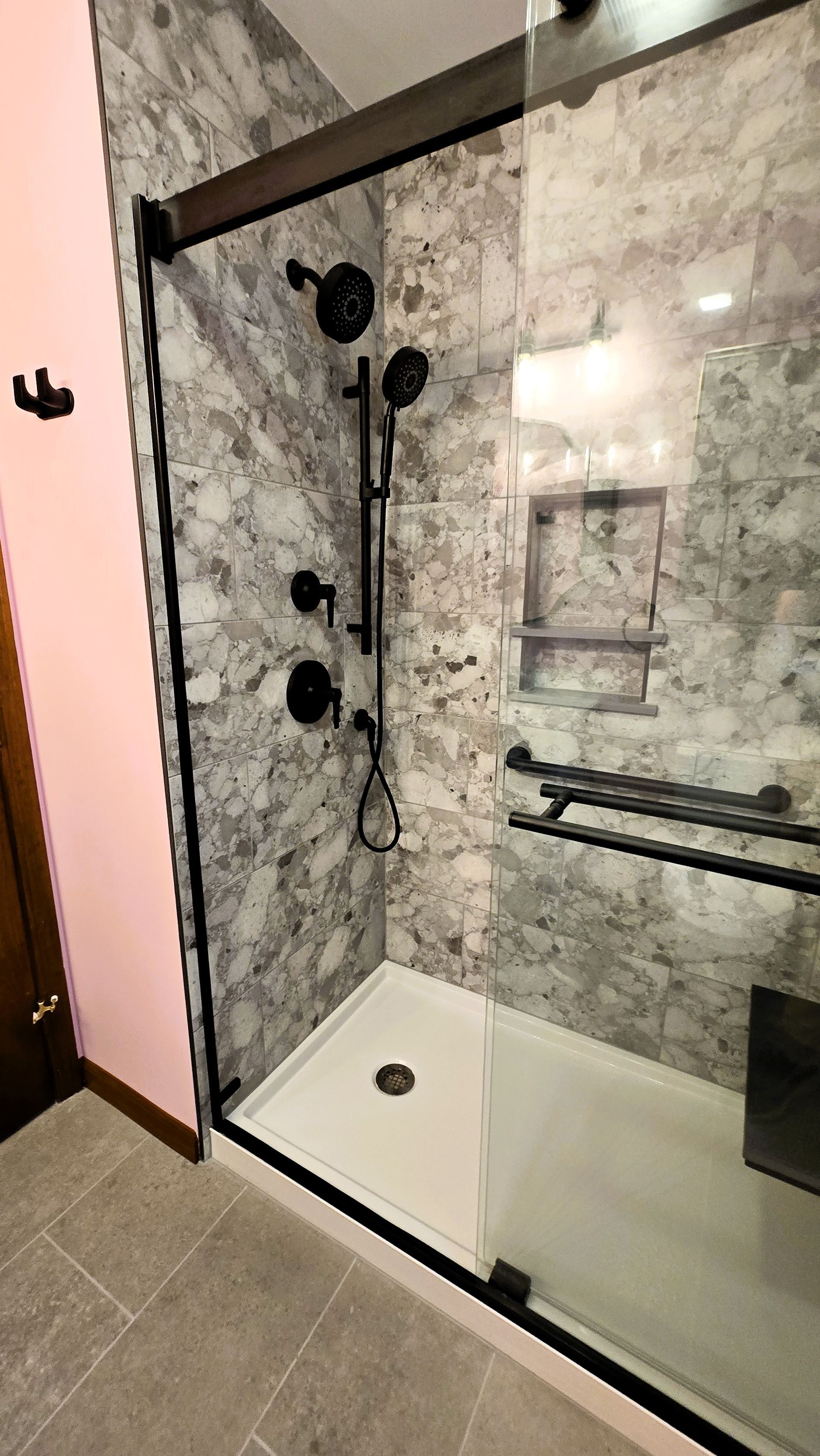 Bathroom shower with marble-like tile, black fixtures, glass door, and a built-in bench.