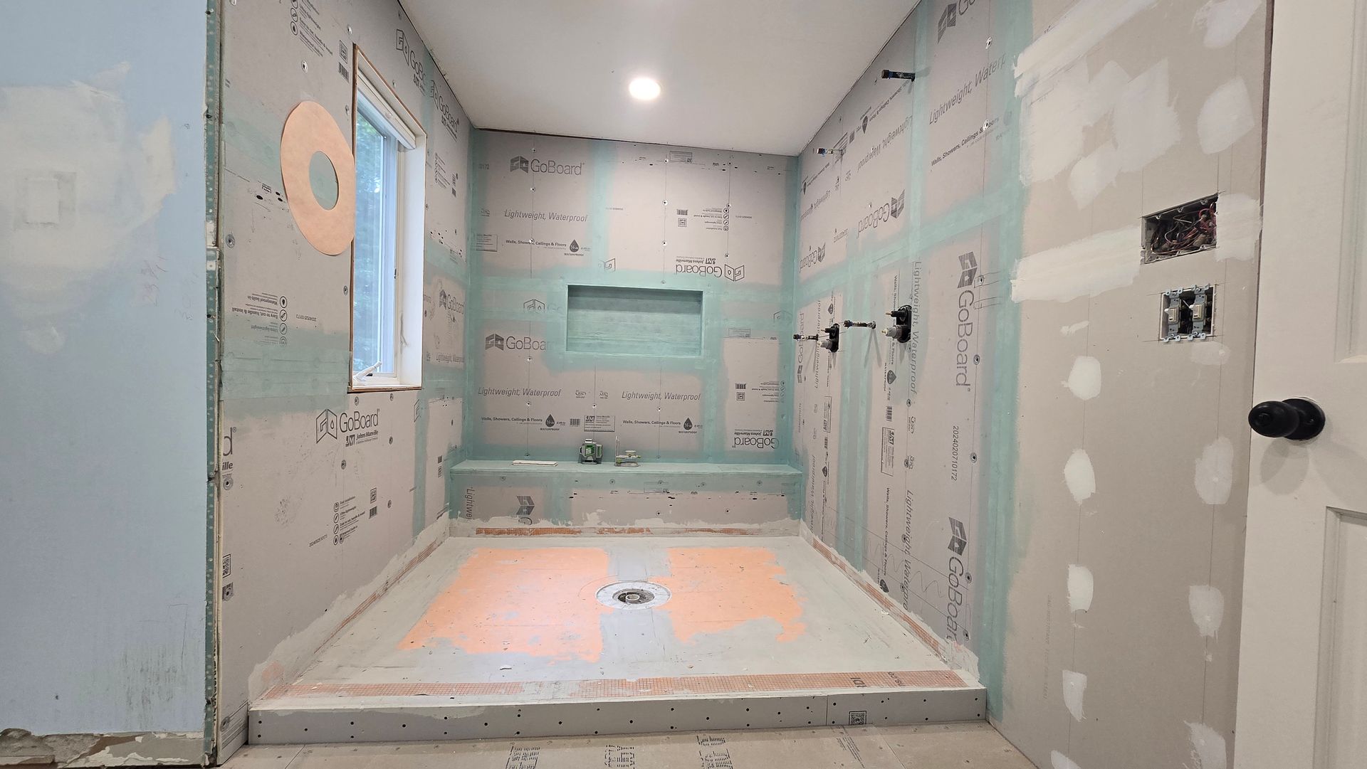 A bathroom under construction with a walk in shower and a window.