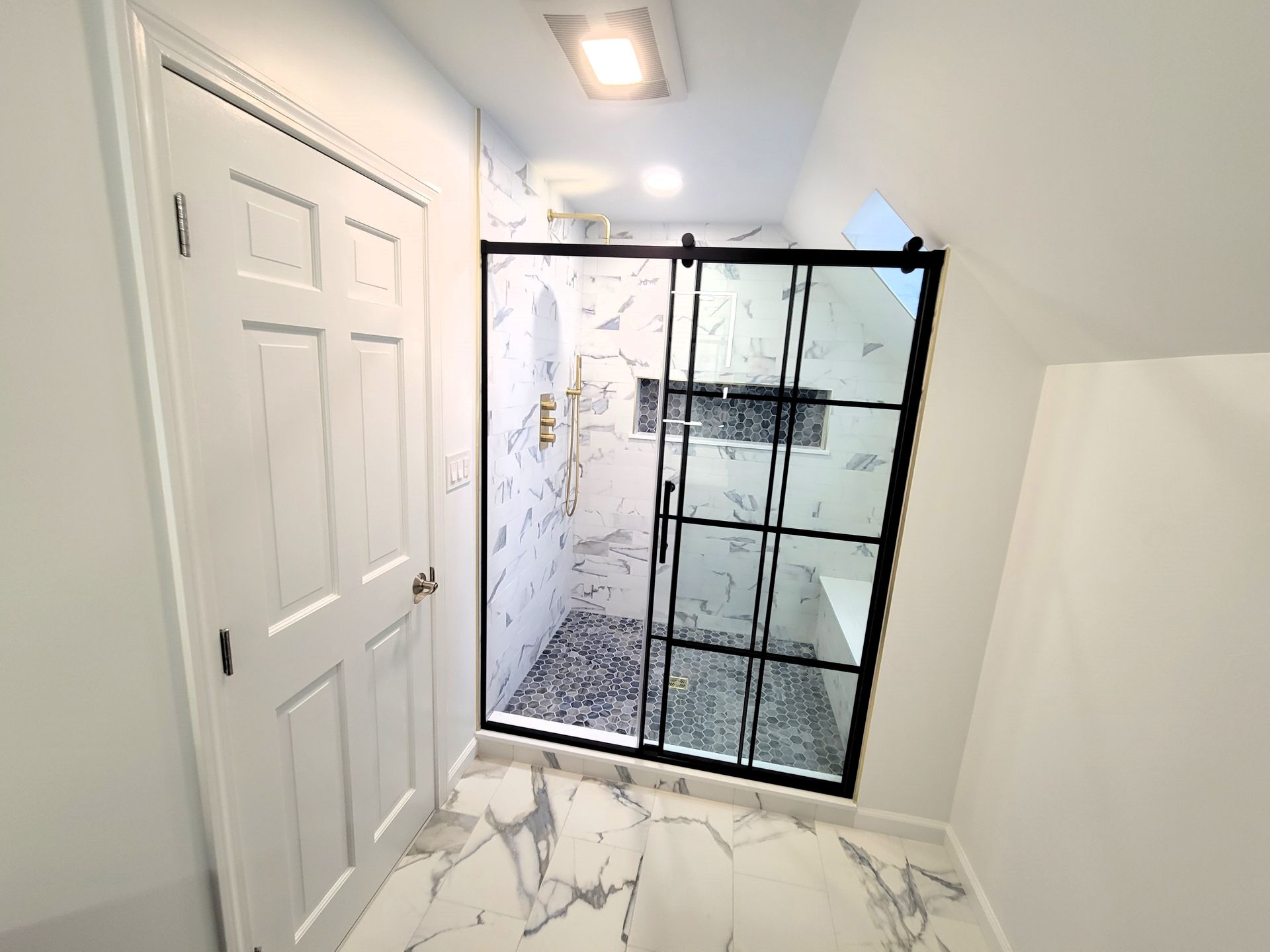 Modern bathroom with marble tile floor, black-framed shower, and white door.