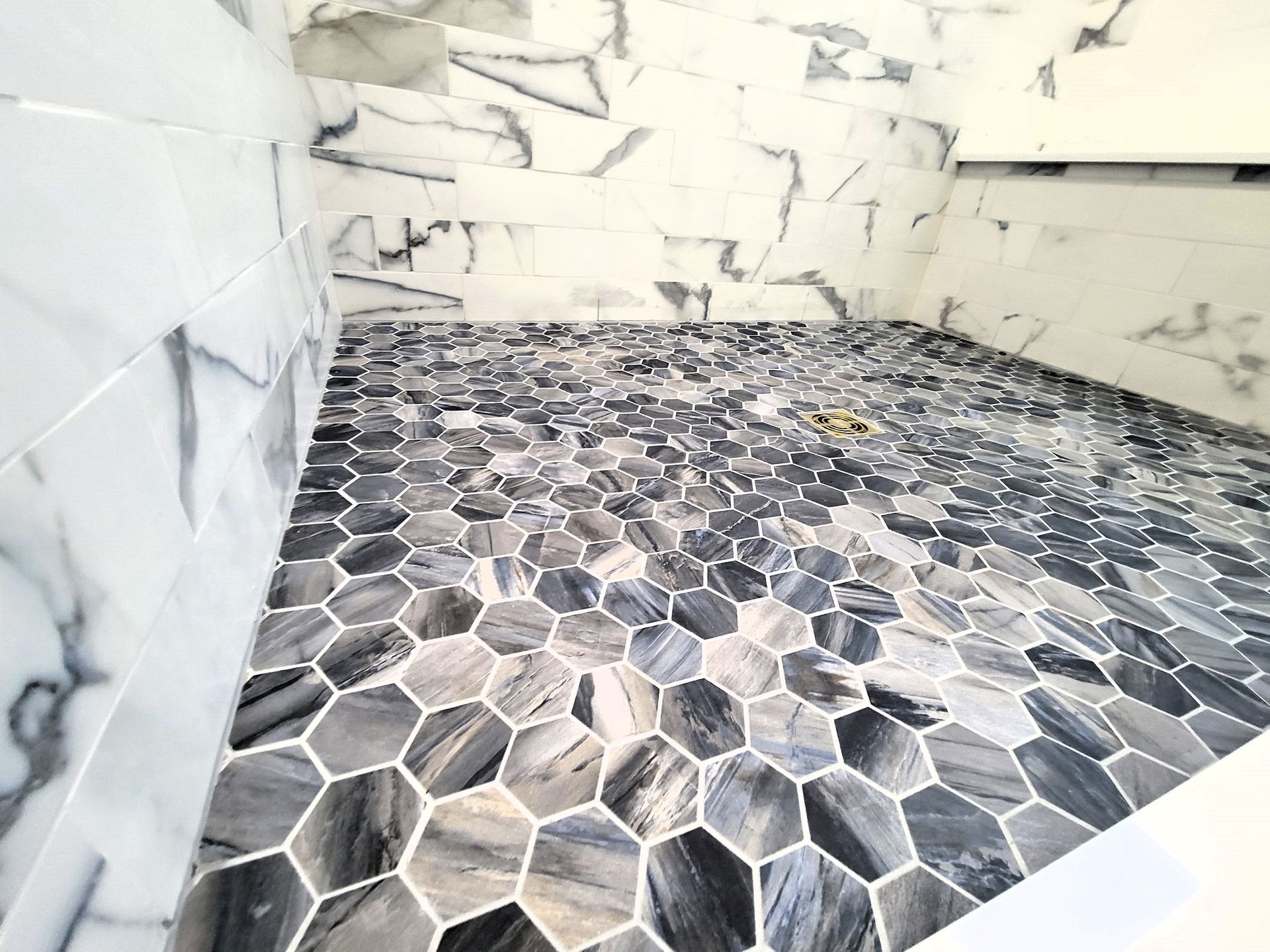 Shower with hexagonal marble floor and marble walls.