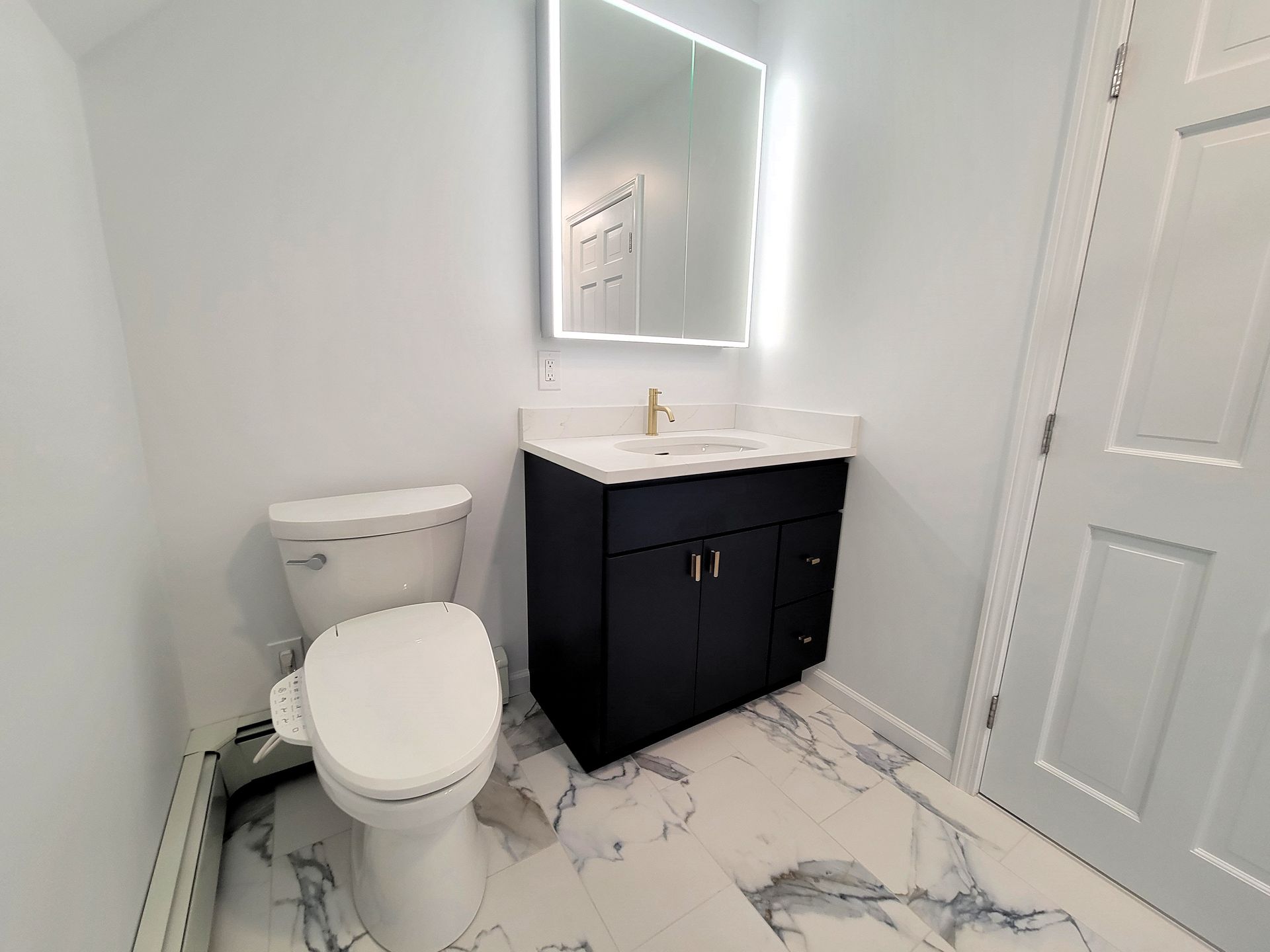 A small, modern bathroom with a dark blue vanity, white toilet, and marble-look flooring.