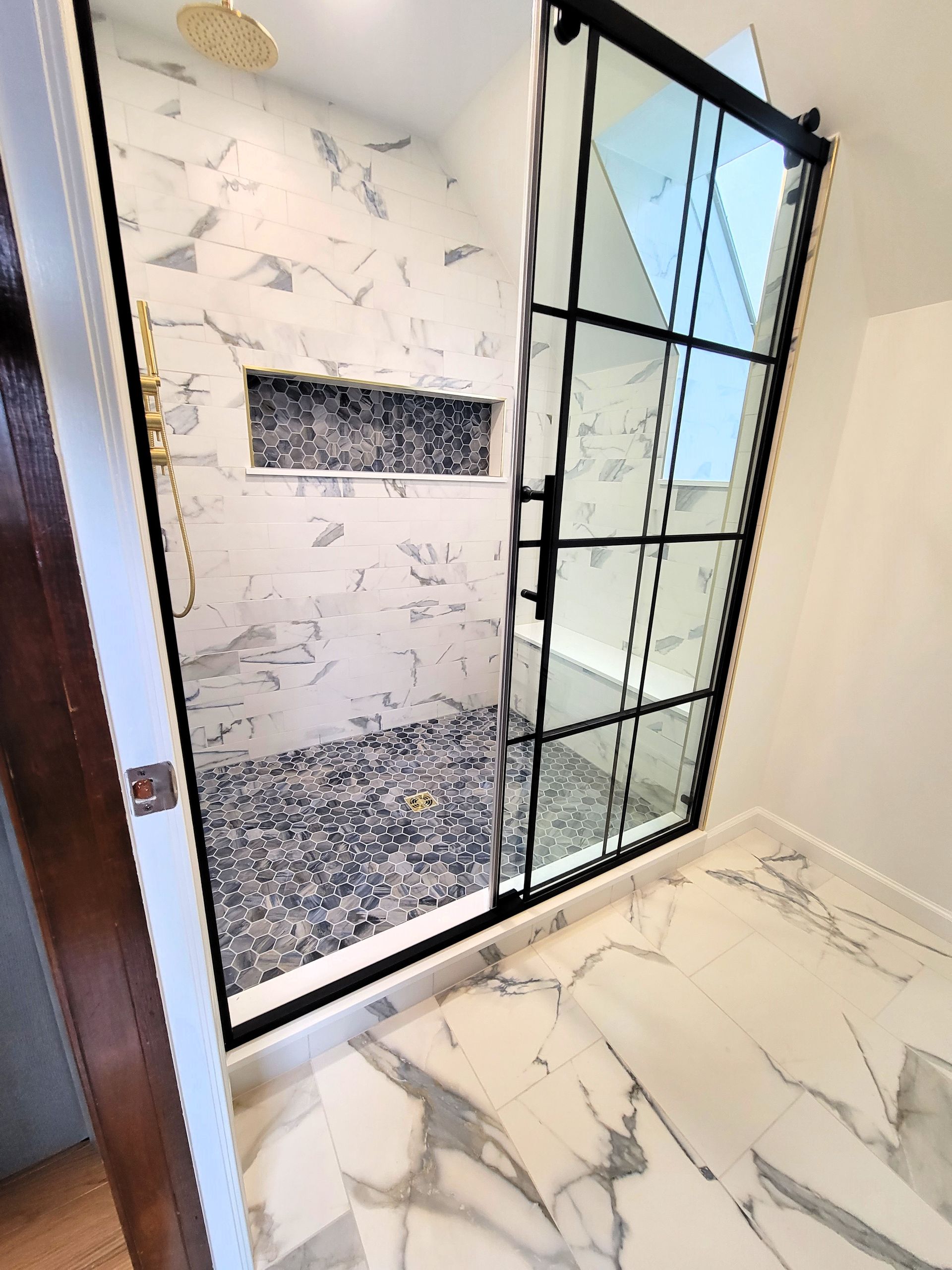 Modern bathroom with marble tile and black framed sliding glass shower door.