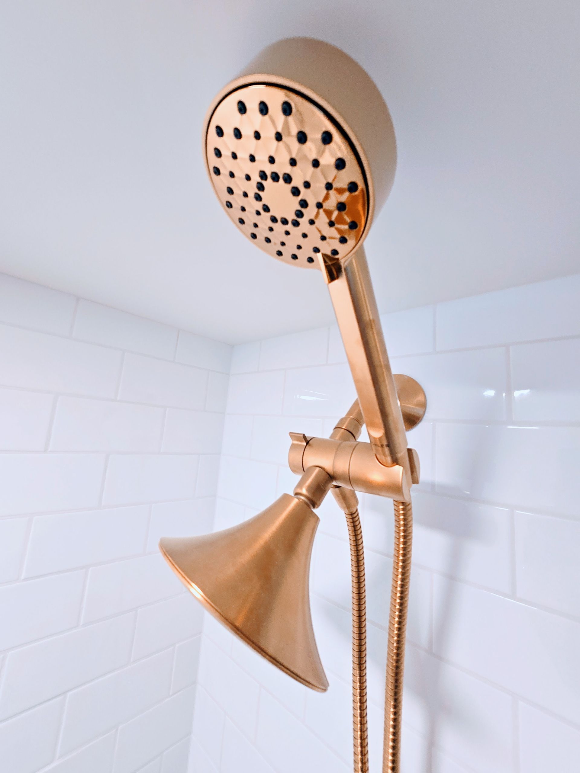 Gold-colored shower head and handheld sprayer against white tiled wall.