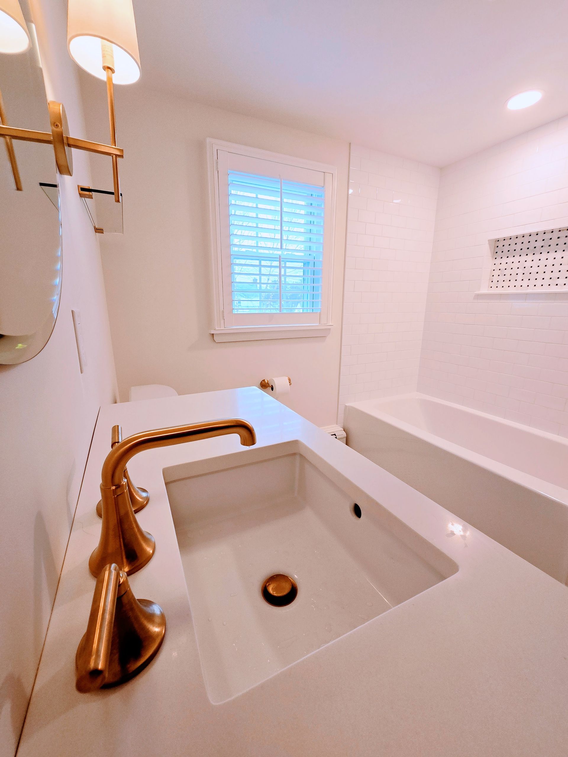 A bathroom with a white sink and a gold faucet