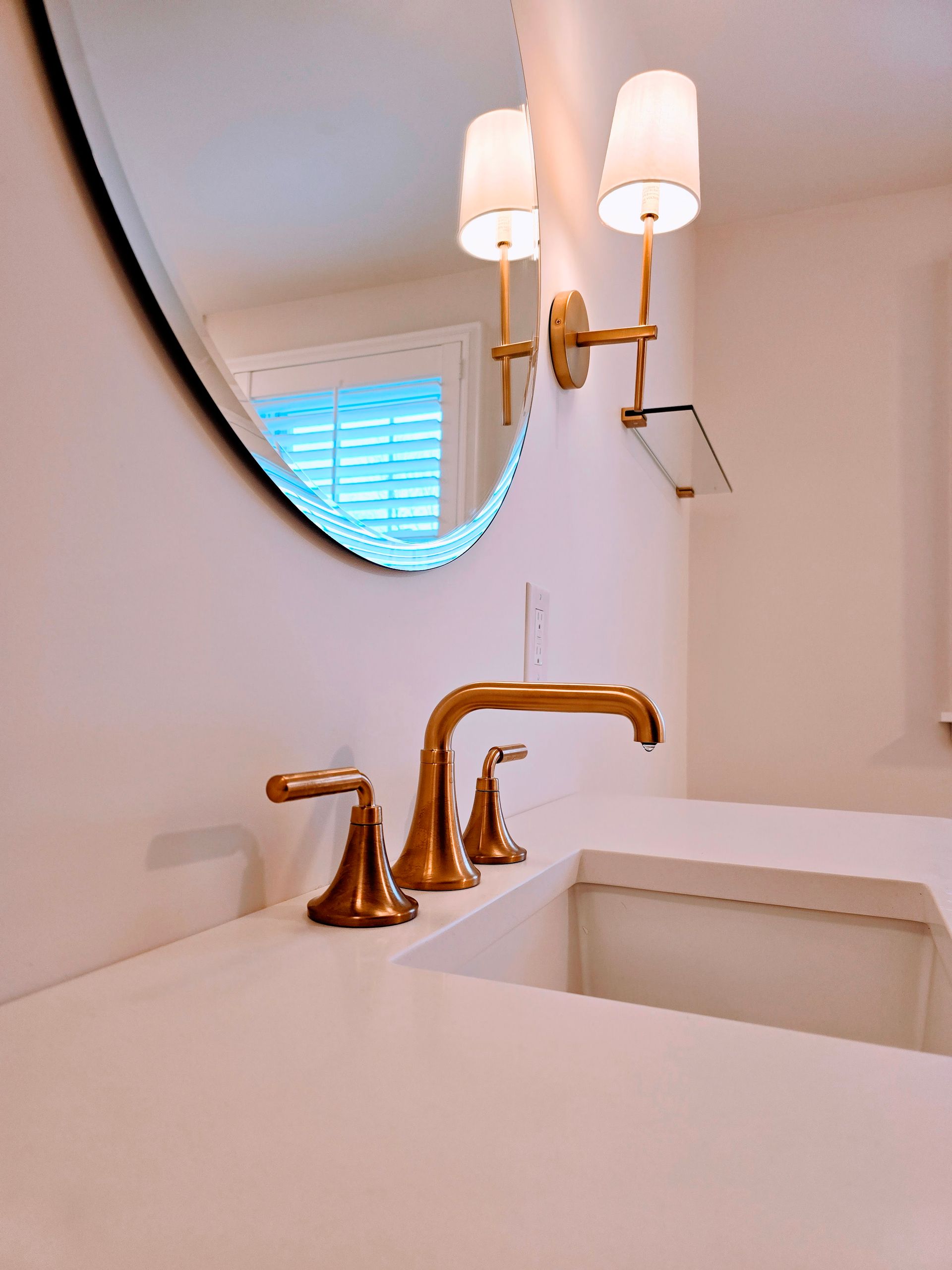 Gold bathroom faucet, sconces, and round mirror above a white countertop.
