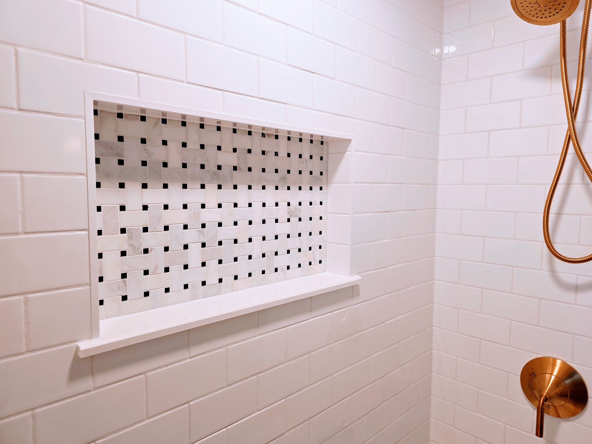 A bathroom with white tiles and a shower head.