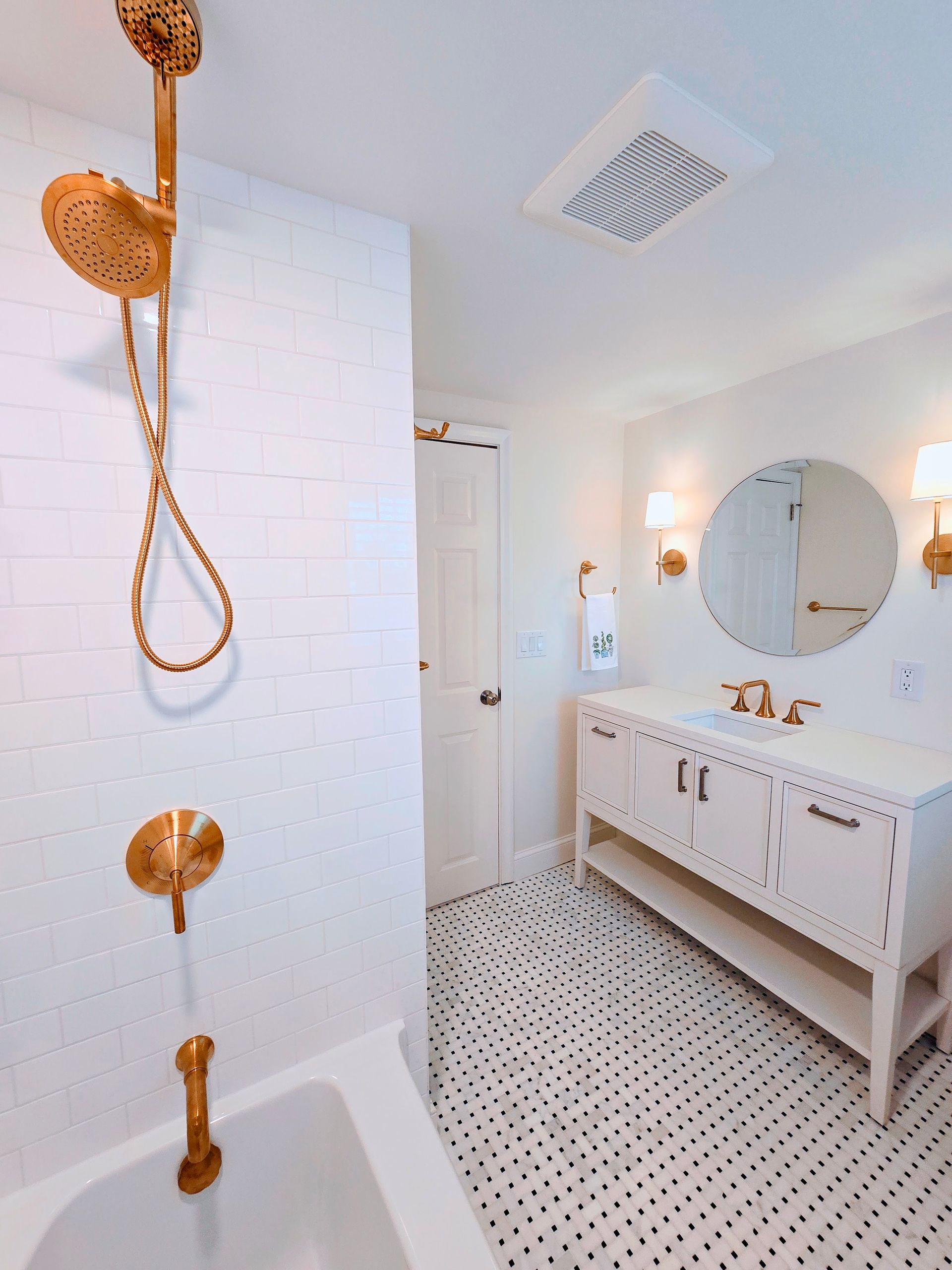Gold shower fixtures in a white-tiled bathroom with a patterned floor and white vanity.