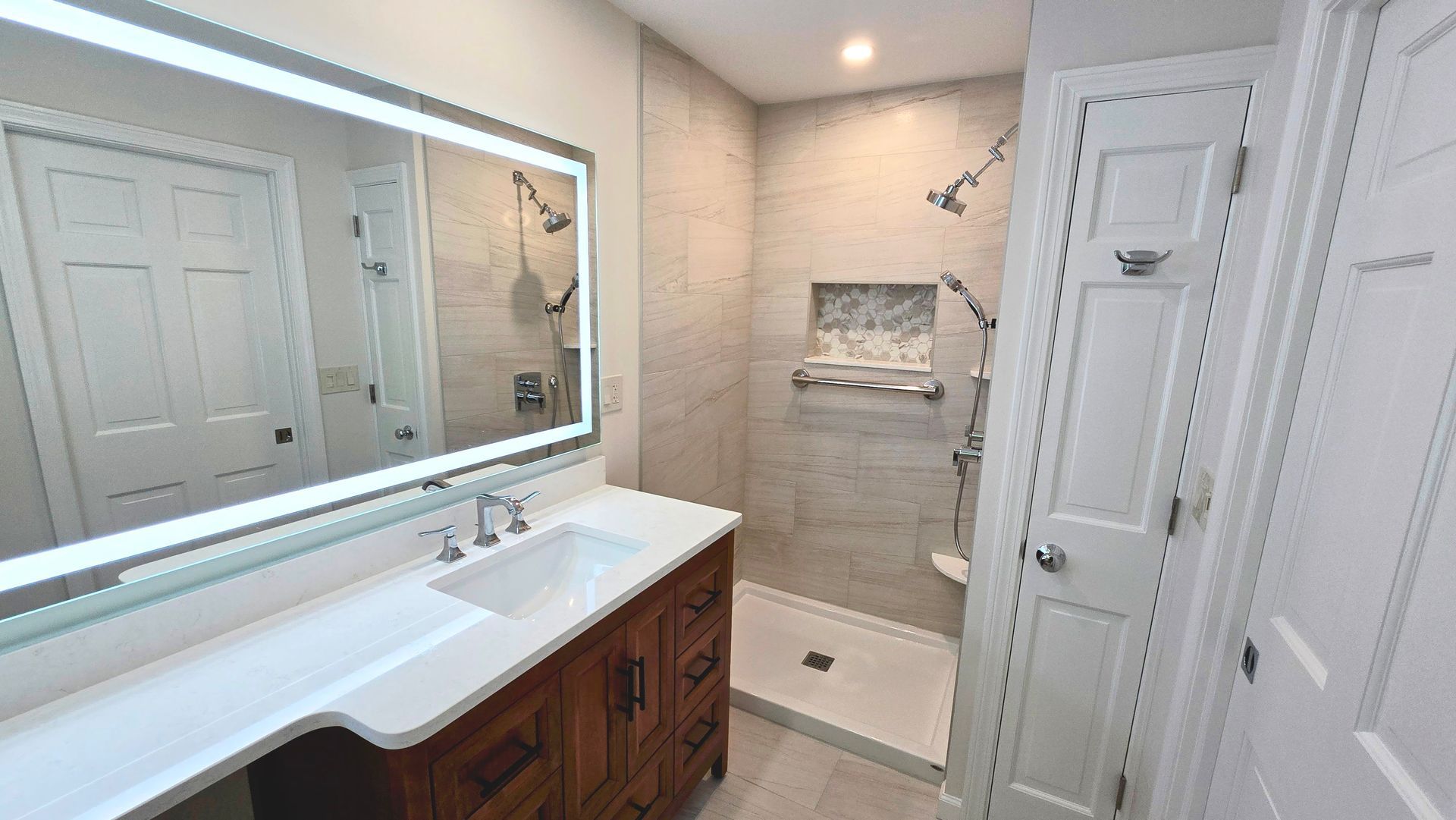 A bathroom with a sink , mirror and walk in shower.