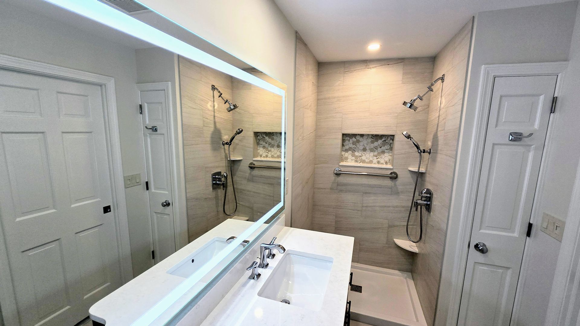 Bathroom with white vanity, tiled shower, and mirrored wall.