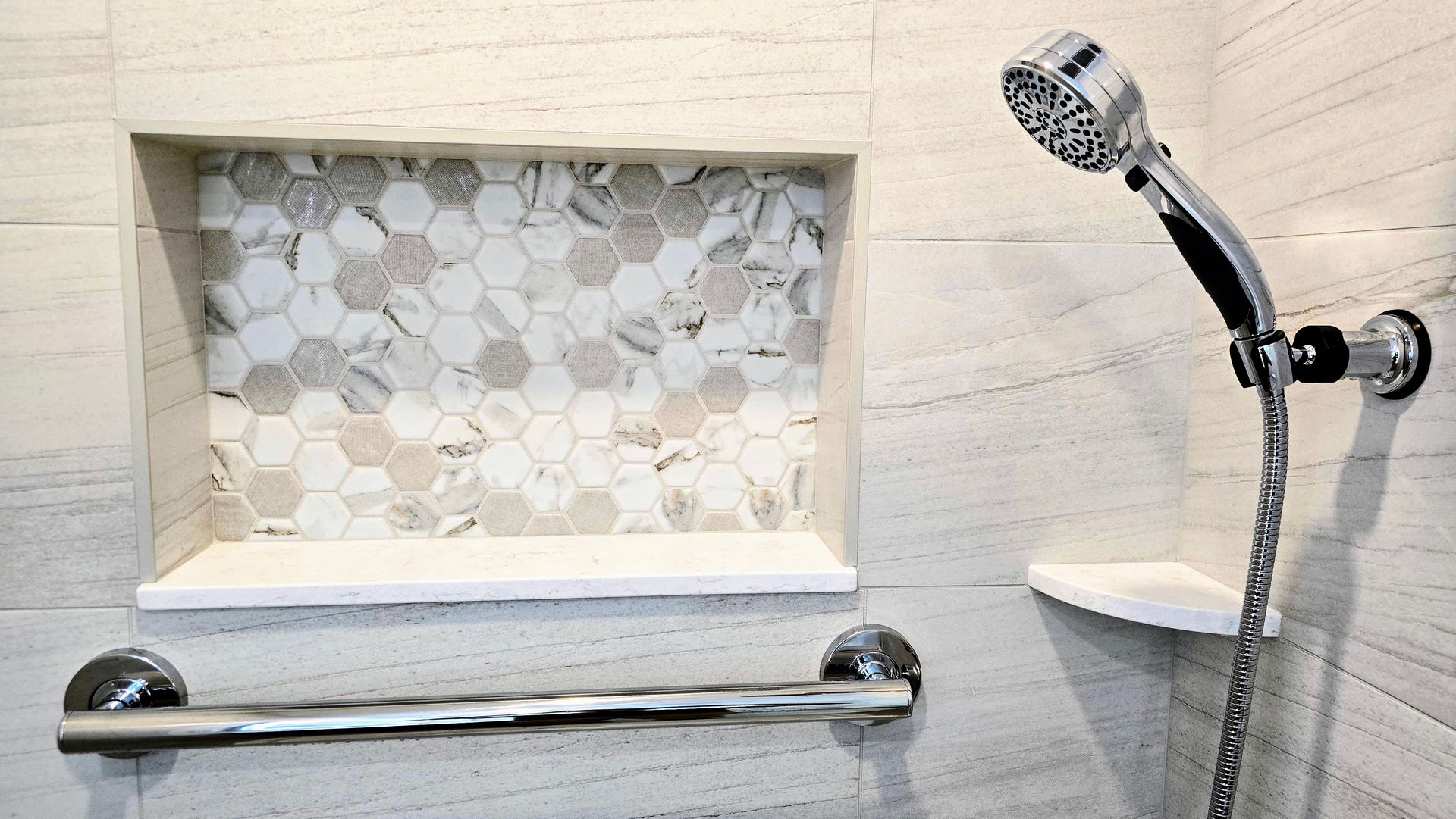 Shower with built-in shelf, patterned tile in recessed area, hand-held shower head, and grab bar.