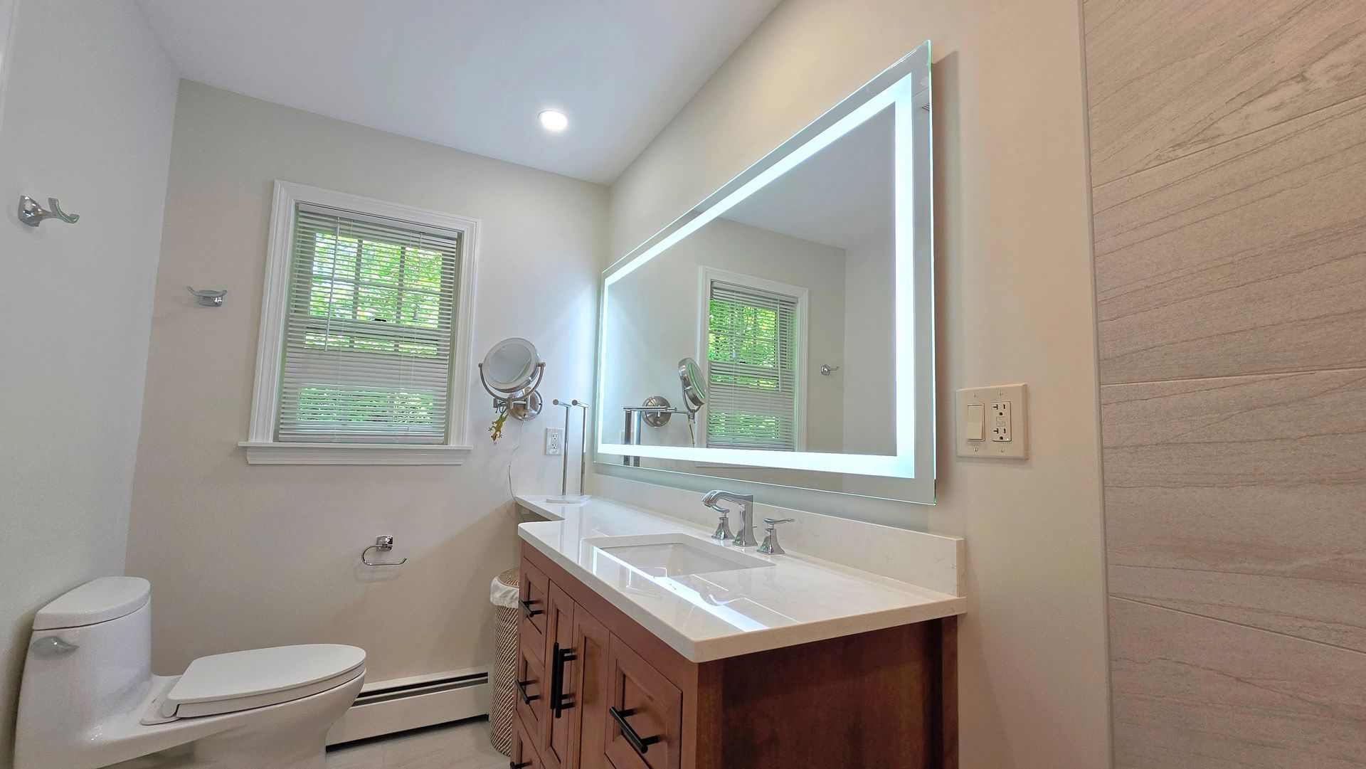 A bathroom with a sink , toilet , mirror and window.
