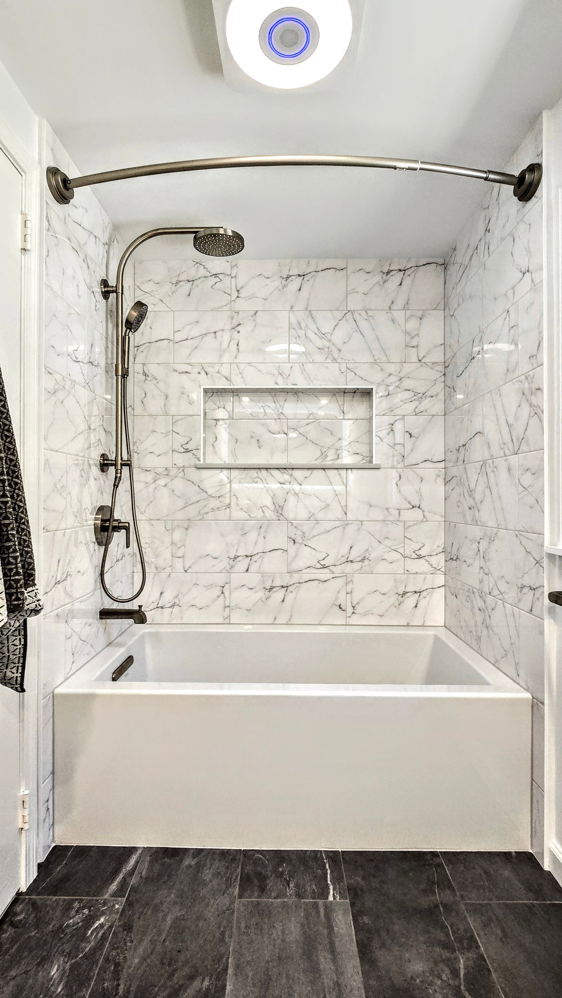 White and marble tiled shower with bathtub in West Hartford, CT and dark flooring.