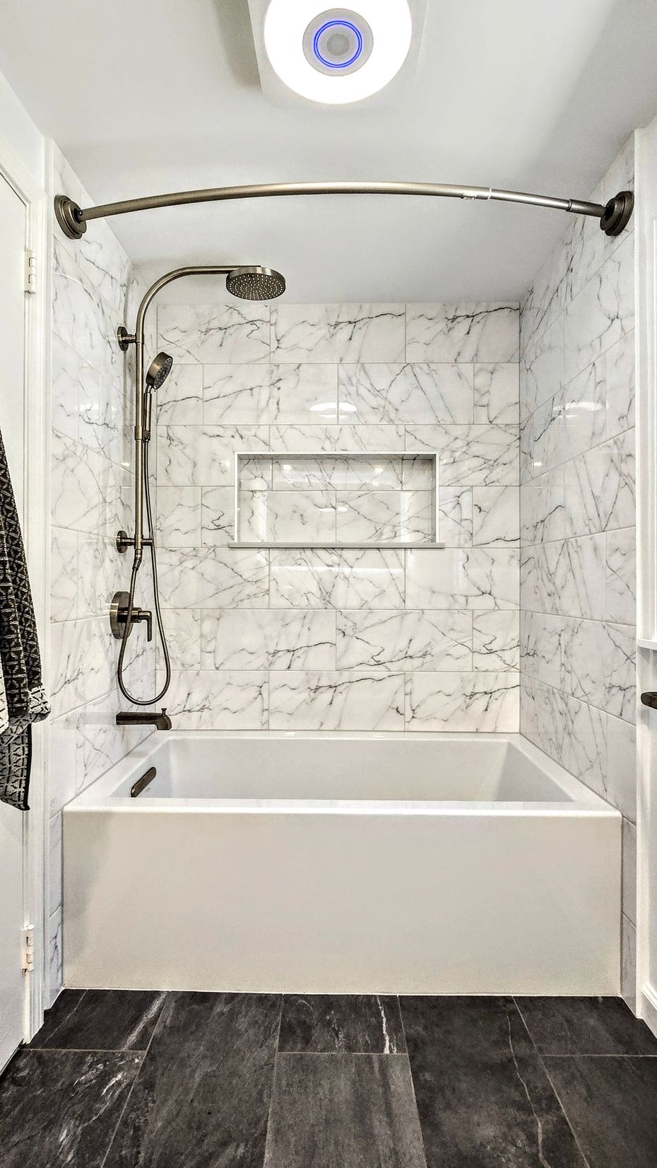 White and marble tiled shower with bathtub in West Hartford, CT and dark flooring.