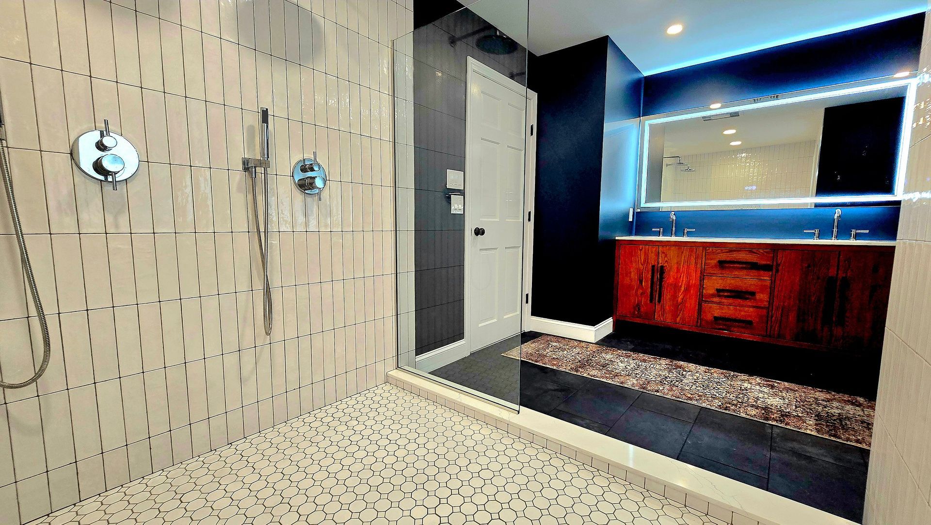 Modern bathroom with walk-in shower, dark blue walls, wooden vanity, and pebble floor.