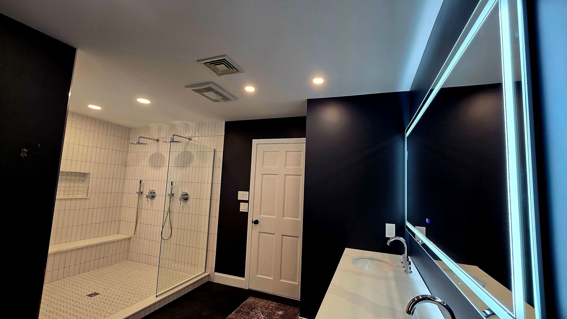 Modern bathroom in Plainville, CT with black walls, white marble shower, lit mirror over the sink.