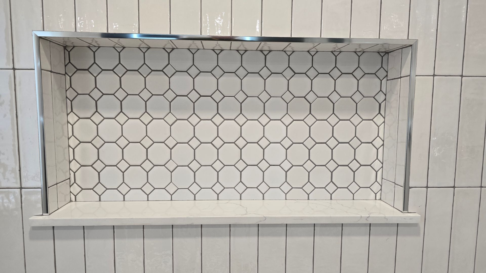 Recessed shower niche with white and patterned tile. Quartz shelf, metallic trim.