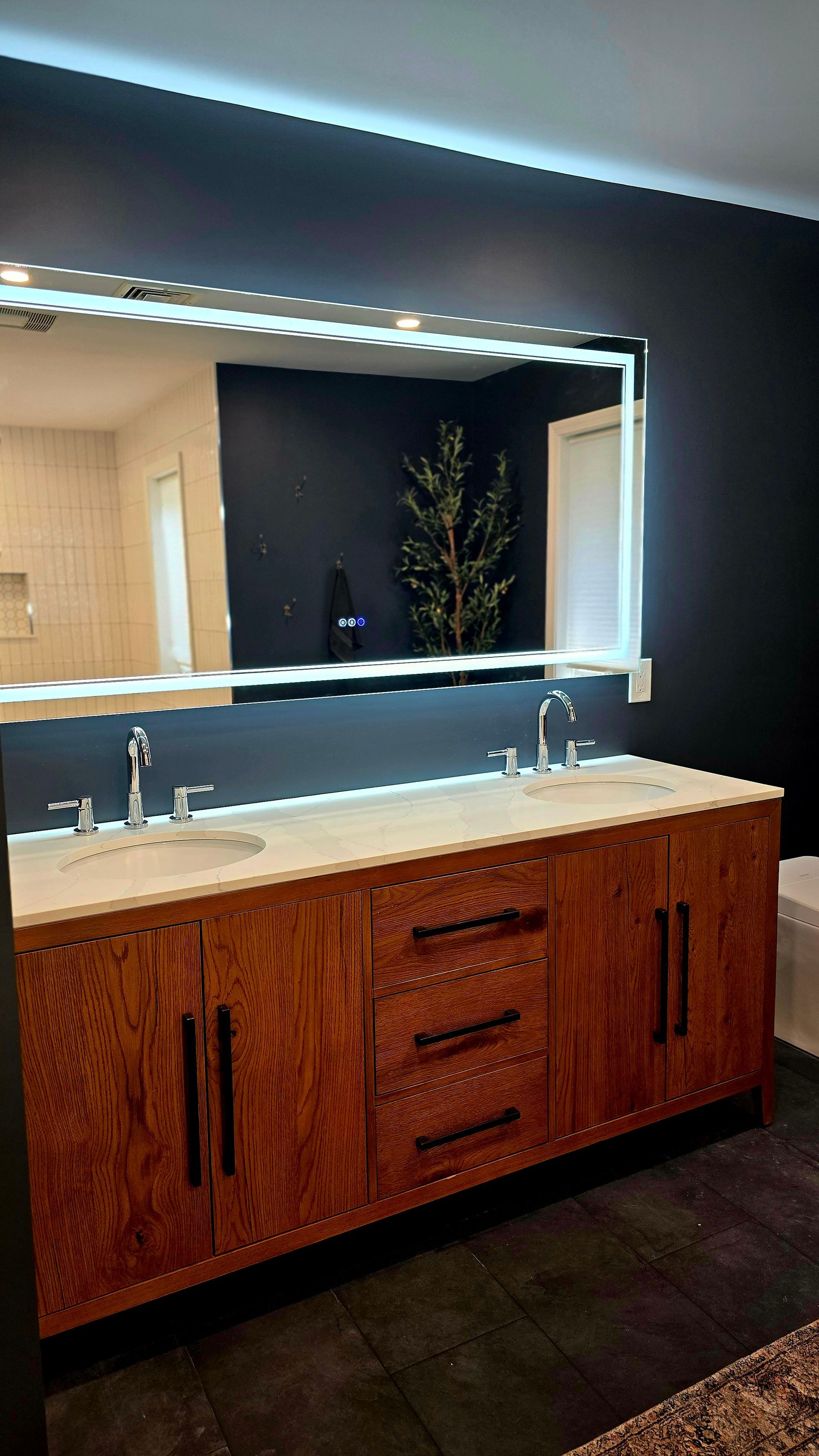 Bathroom with a wood vanity, large mirror with LED lights, and dark walls.