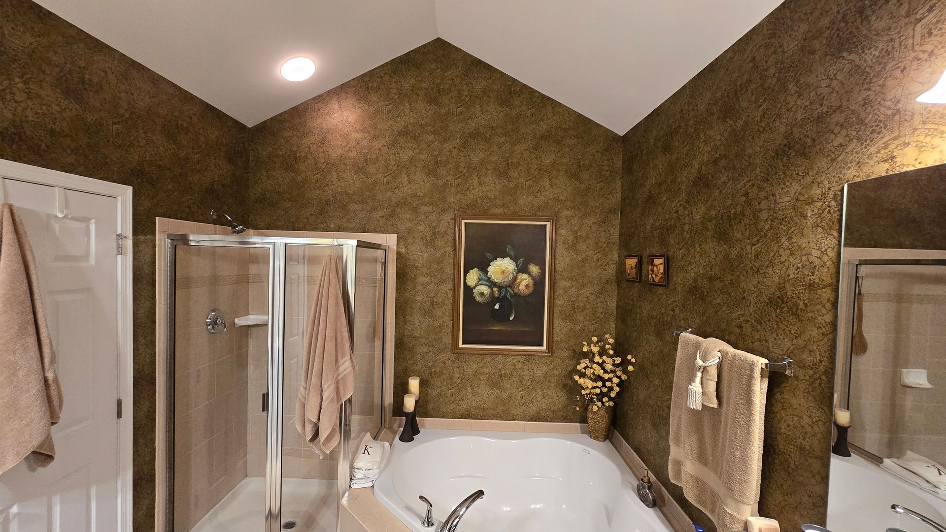 BEFORE Bathroom with a corner tub, glass shower doors, brown textured walls, towels, and framed wall art.