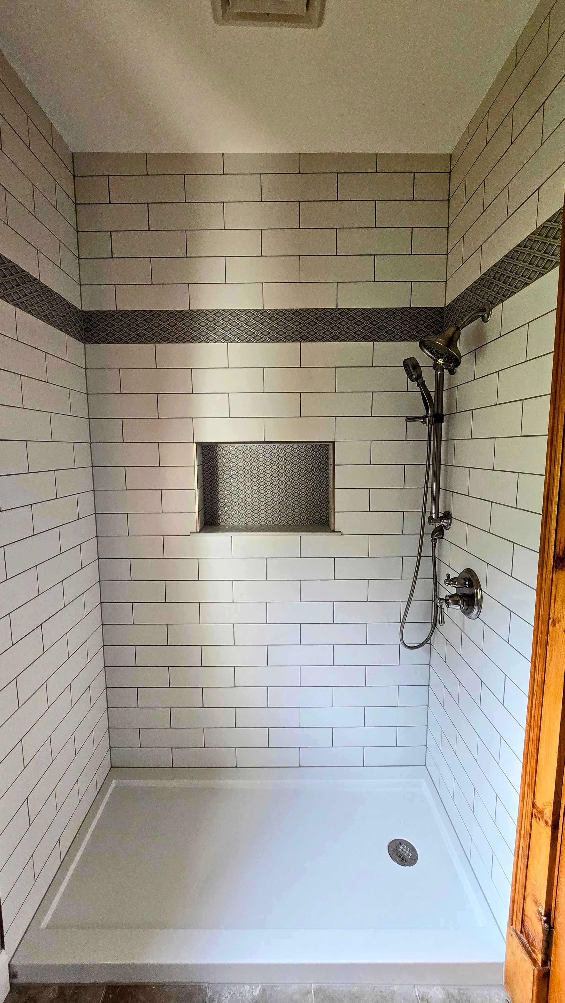 White tiled shower with a dark band of mosaic tile and a built-in niche; showerhead and controls.
