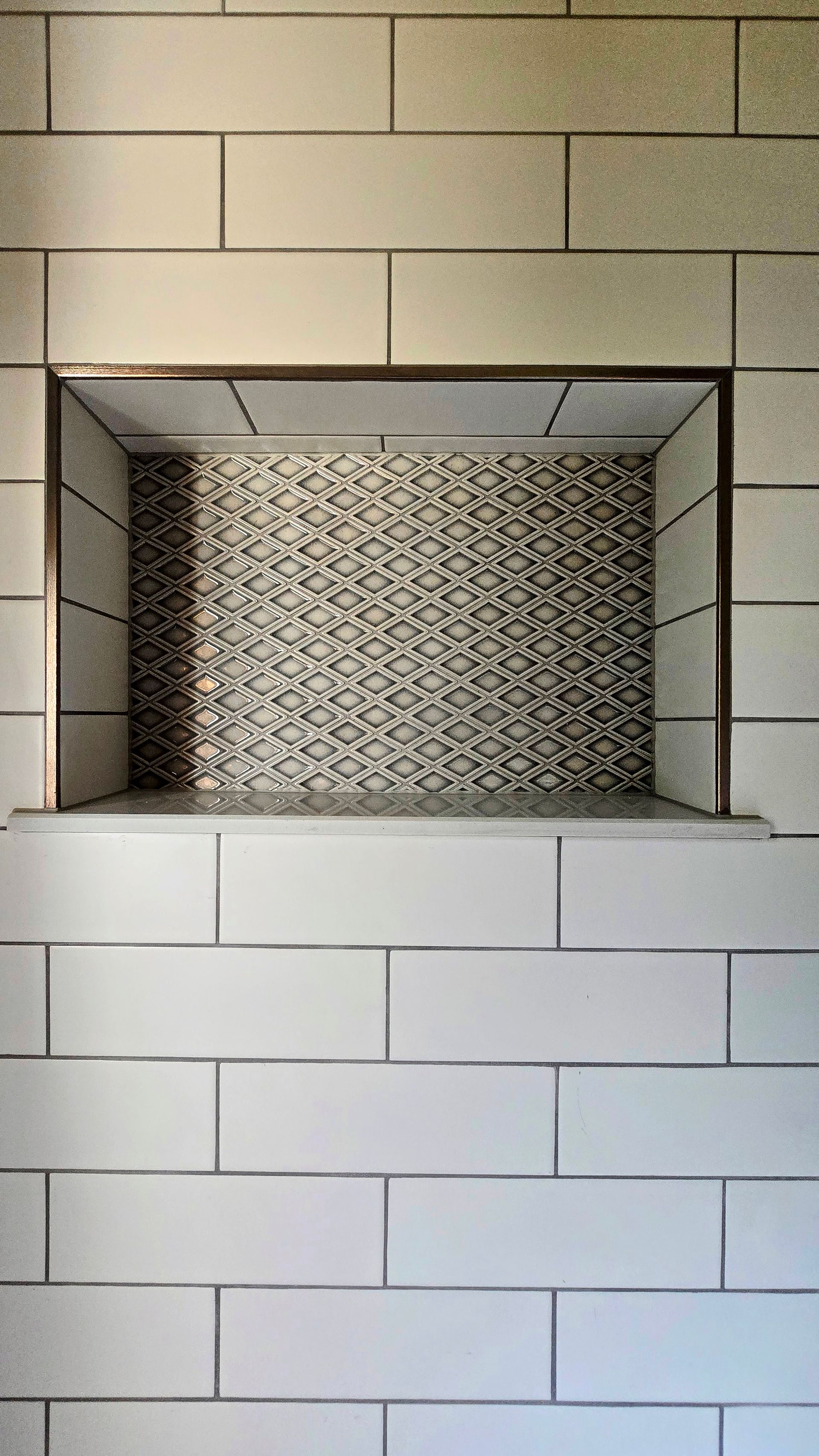 Recessed shower niche with mosaic tile background, framed by white subway tile.