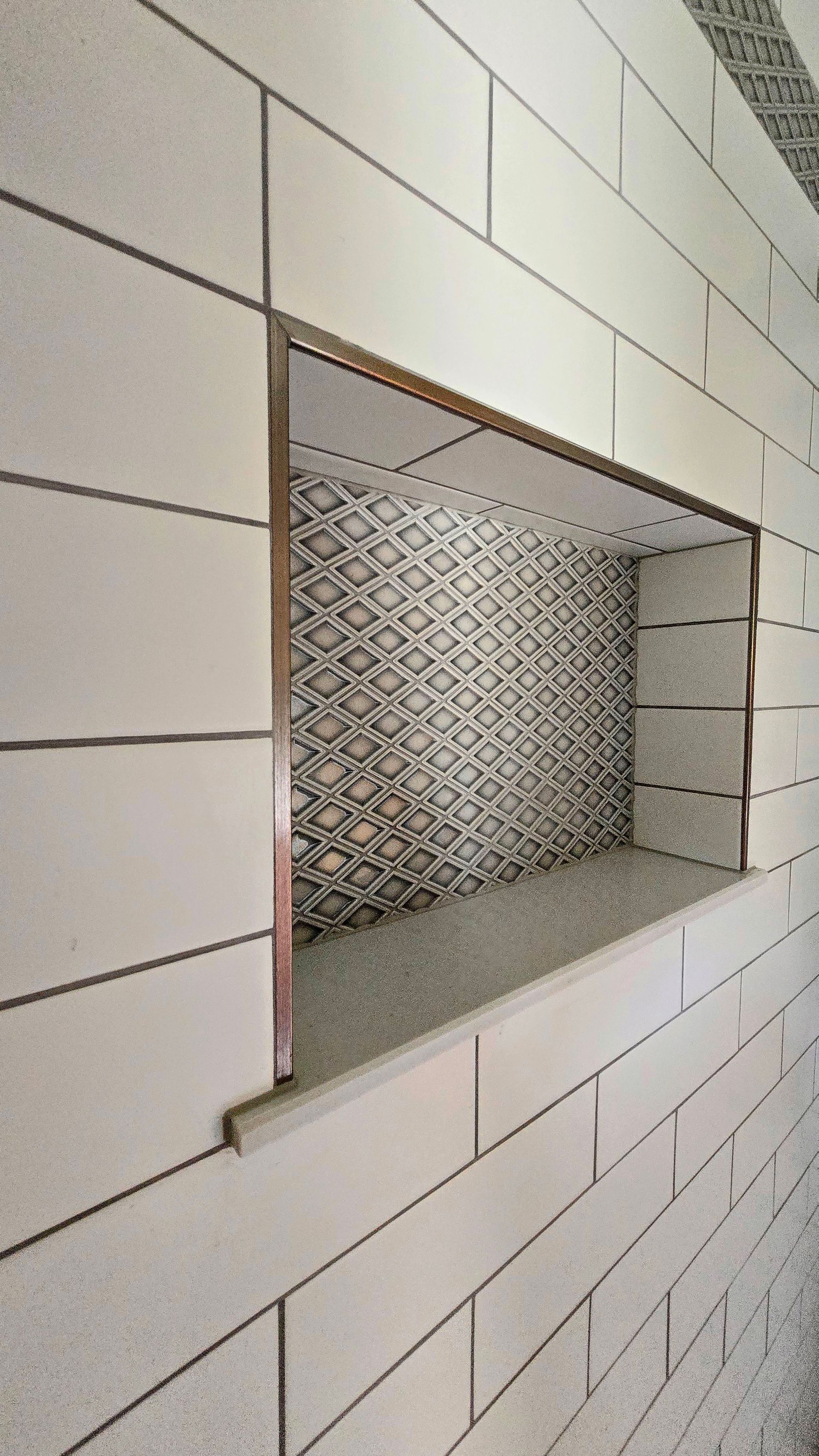 Recessed shelf in a tiled wall, with a patterned interior. White tiles surround a decorative space.