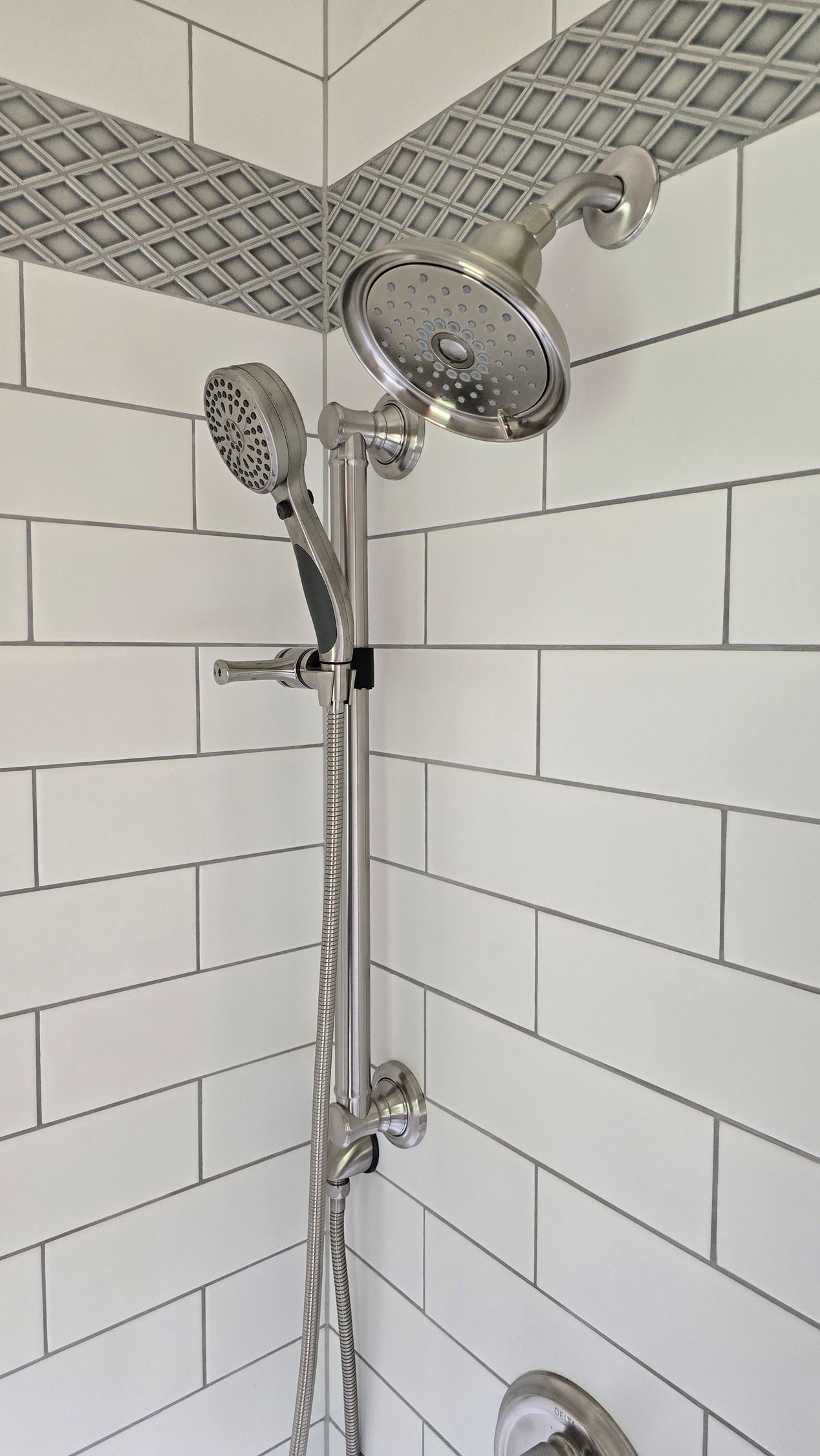 A close up of a shower head in a bathroom with white tiles.