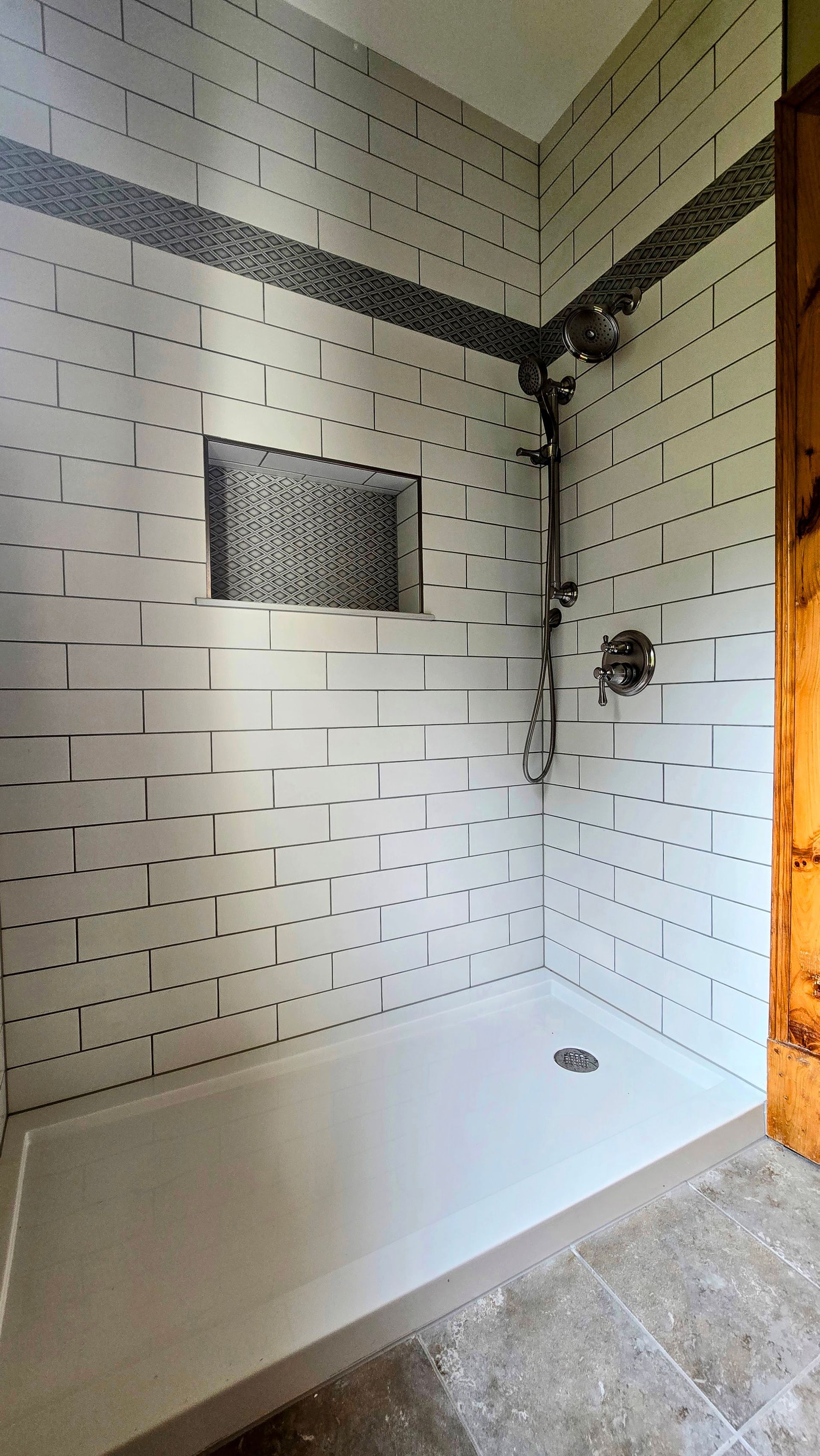 Modern shower with white subway tiles, mosaic accent band, and built-in shelf.