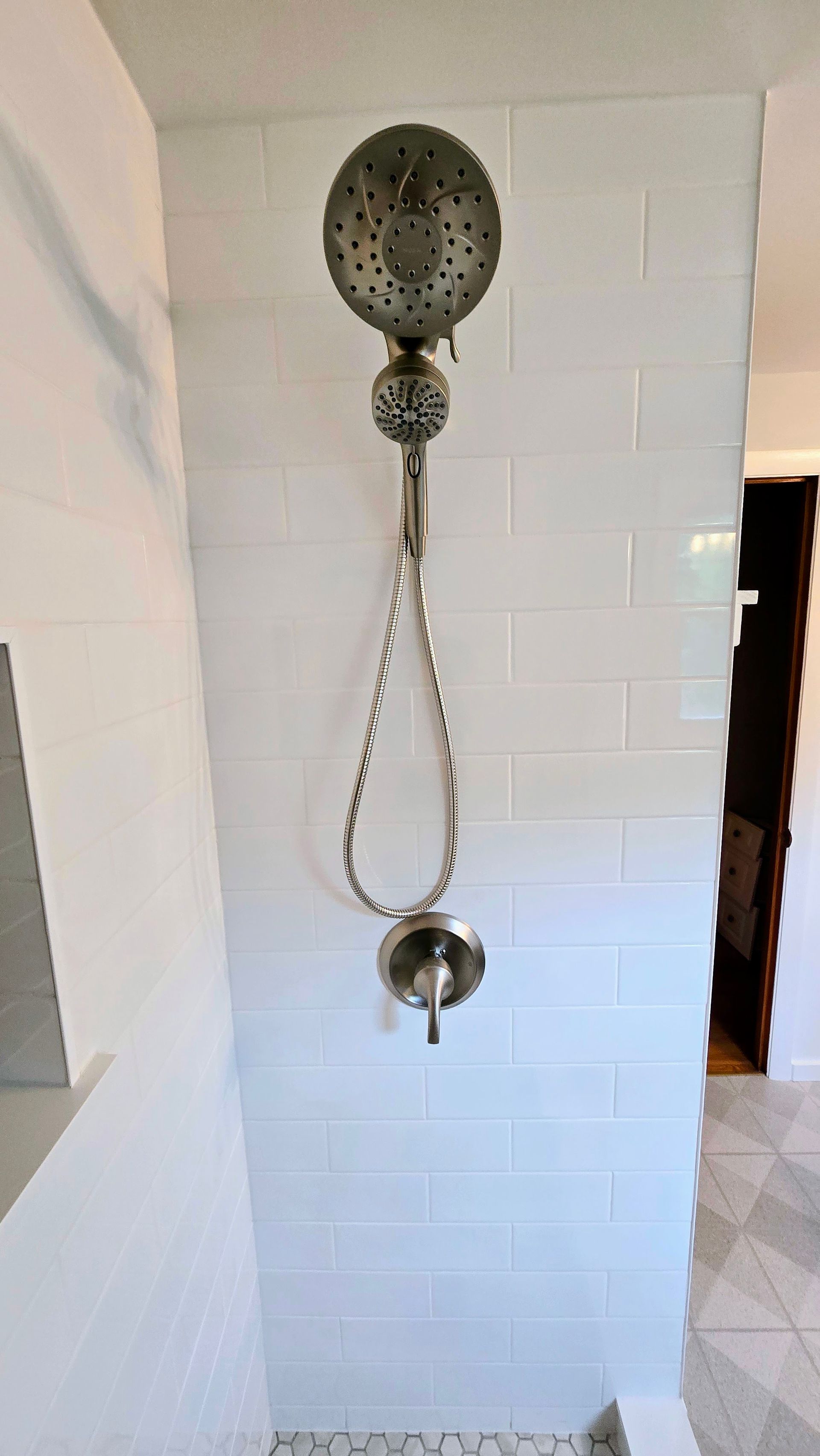 A shower head is hanging from a white tiled wall in a bathroom.