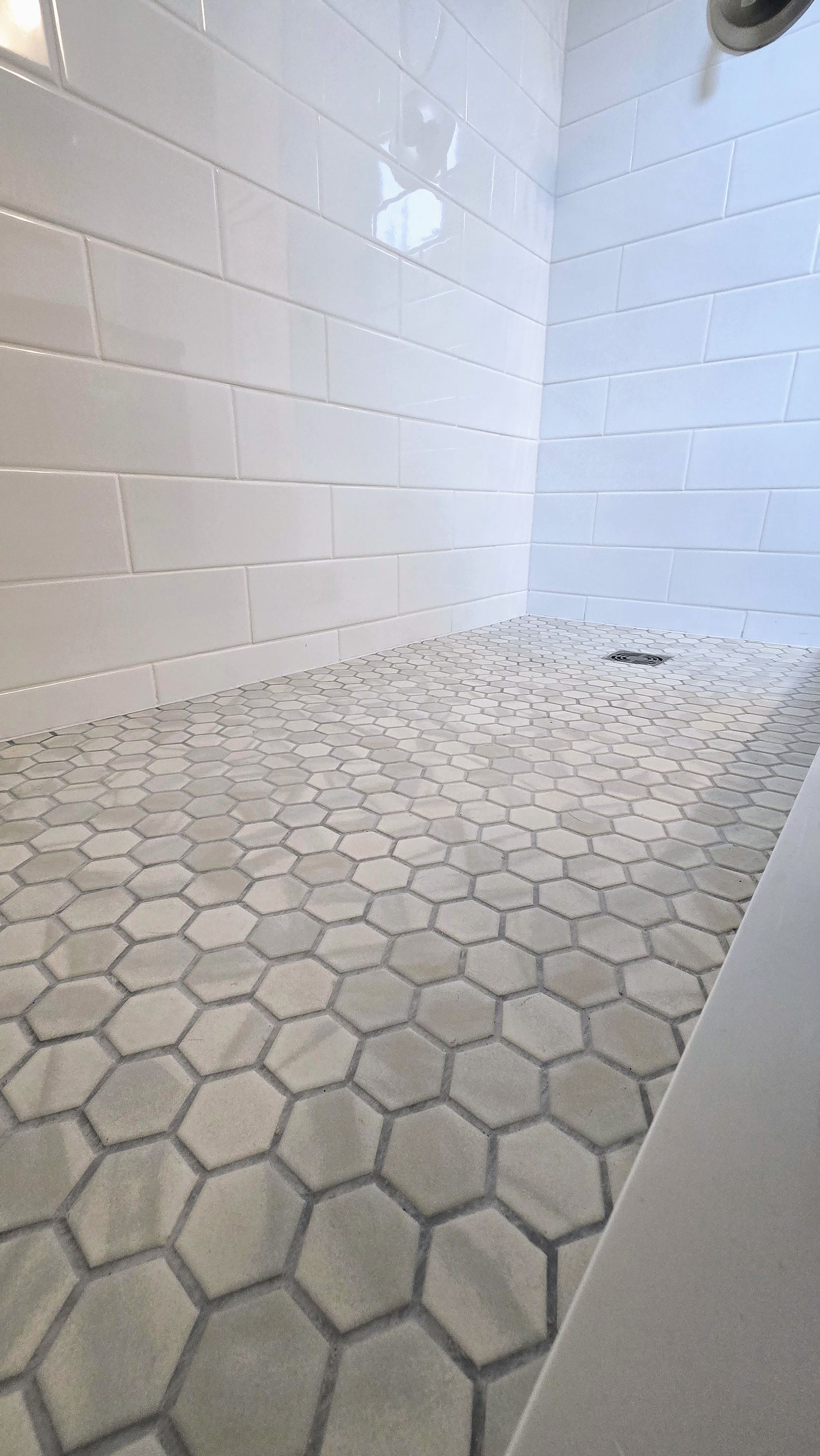 A shower with a honeycomb tile floor and white brick walls.