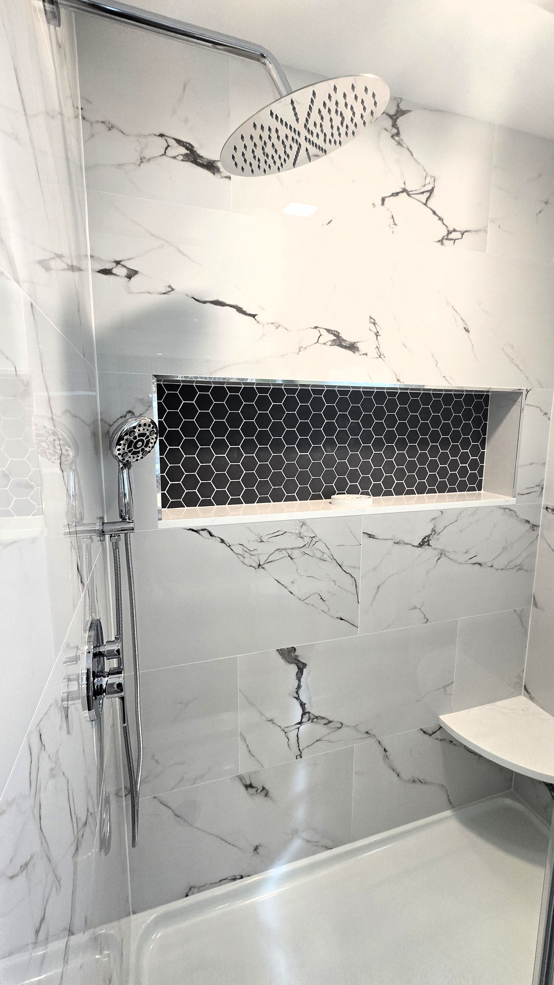 Shower with white marble tile and black tile niche. Silver shower head and fixtures, white seat.