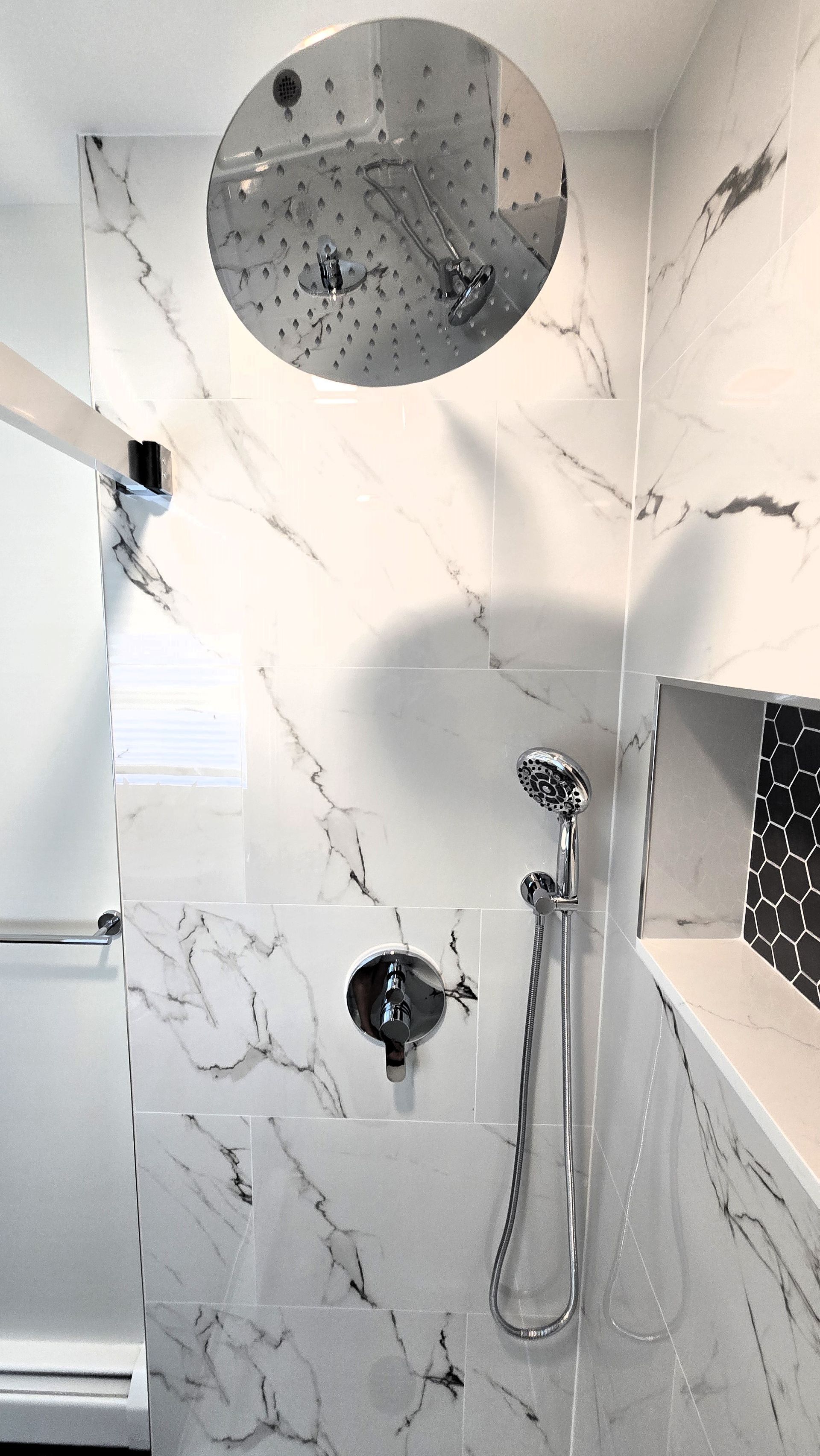 A bathroom with a shower head and a marble wall.