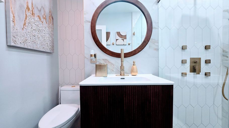 Bathroom in East Hartford, CT with dark wood vanity, round mirror, white and gold tile, gold fixtures.
