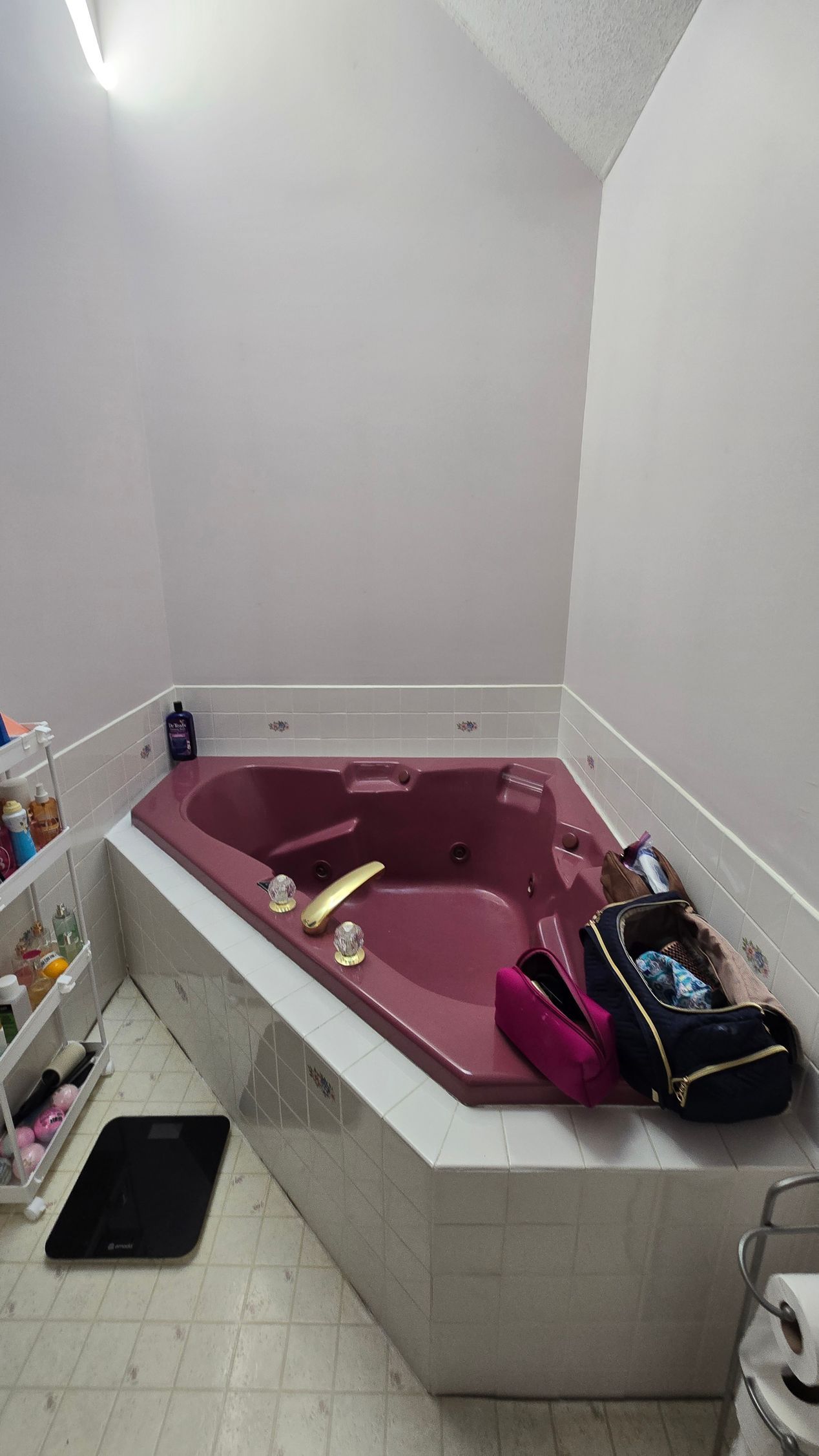 A burgundy corner jacuzzi tub in a white-walled bathroom. A black scale and toiletries are visible.