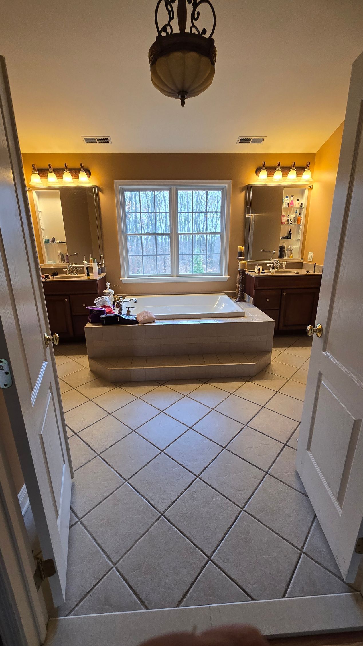 A bathroom with a tub , sinks , mirrors and a window.