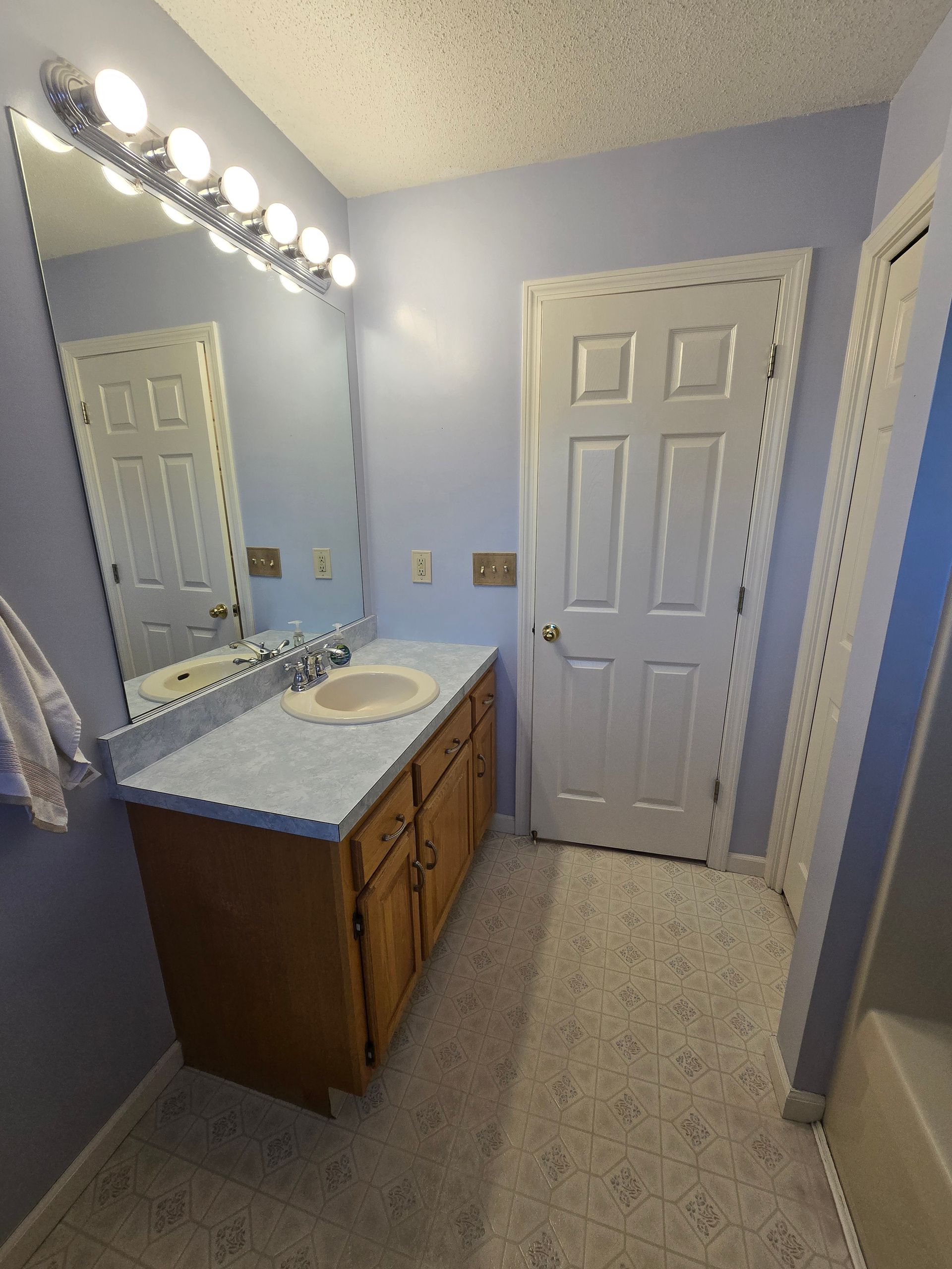 Bathroom with blue walls, white door, vanity with mirror, and patterned floor.