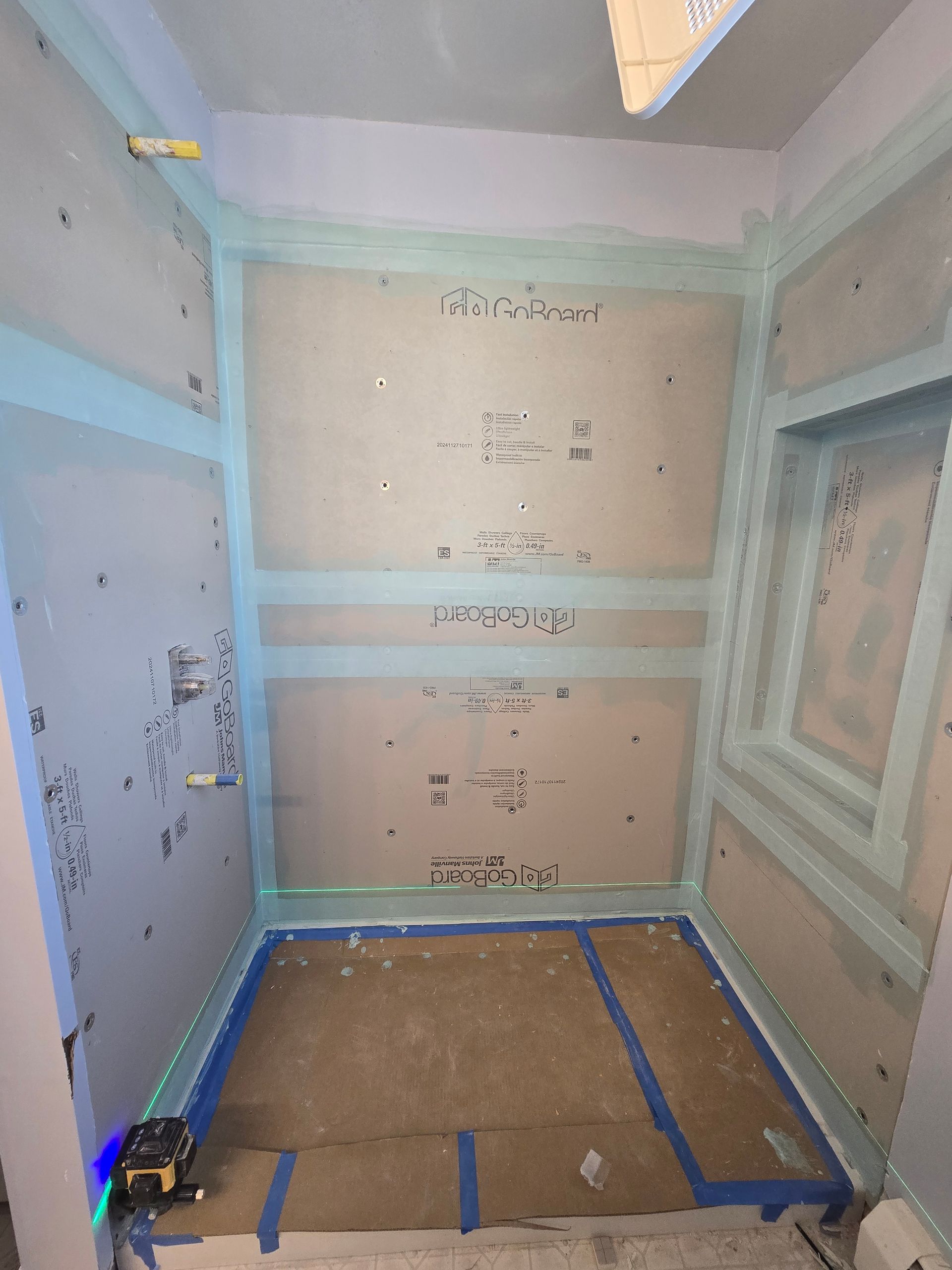Shower stall under construction: walls with blue tape, green sealant. Laser level on floor.