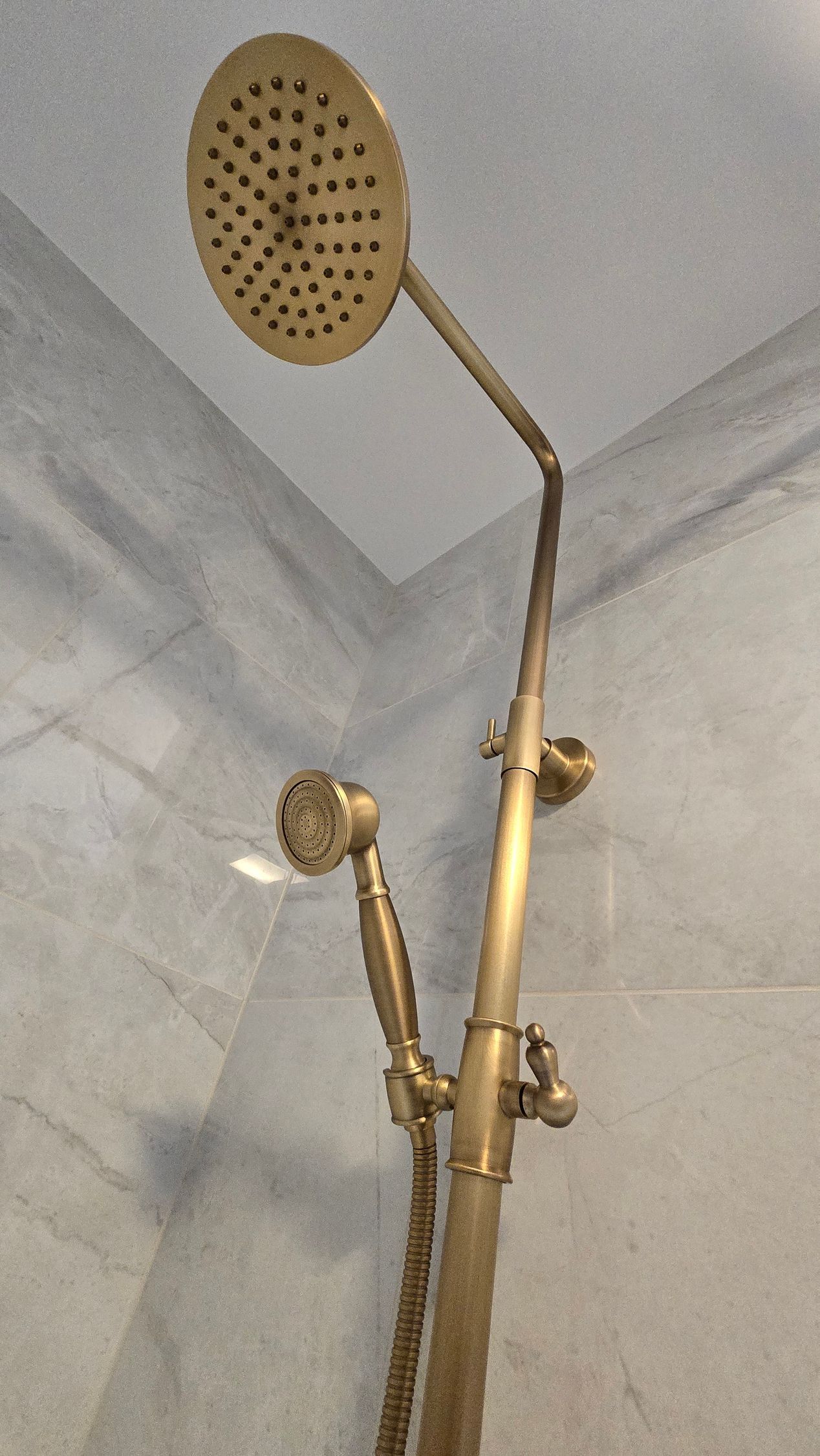 Bronze shower head with handheld nozzle against a tiled wall.