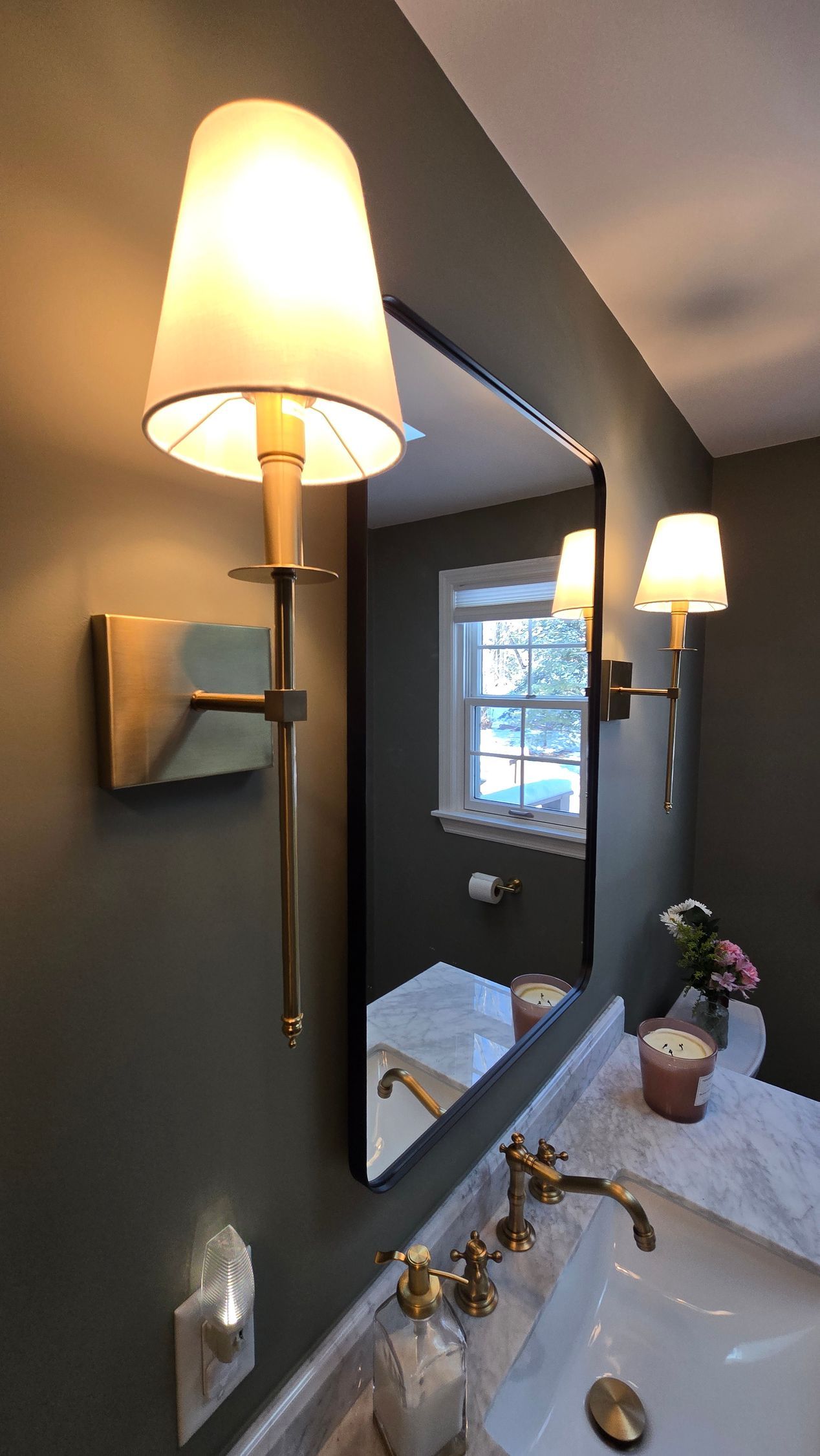 Bathroom with gold sconces flanking a mirror above a white sink and marble countertop.