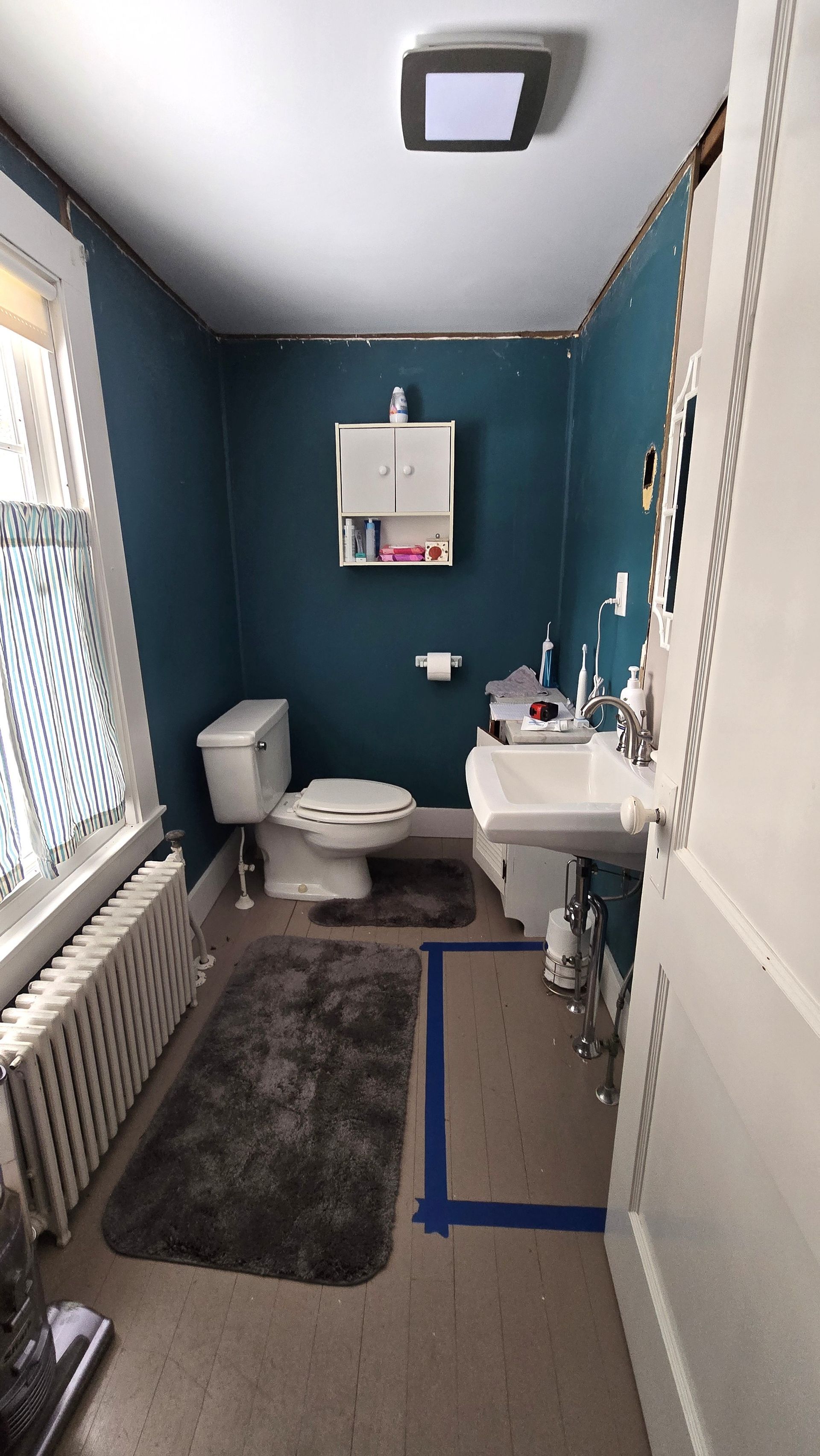 Small teal bathroom with toilet, sink, mirror, bathtub, and gray rug.
