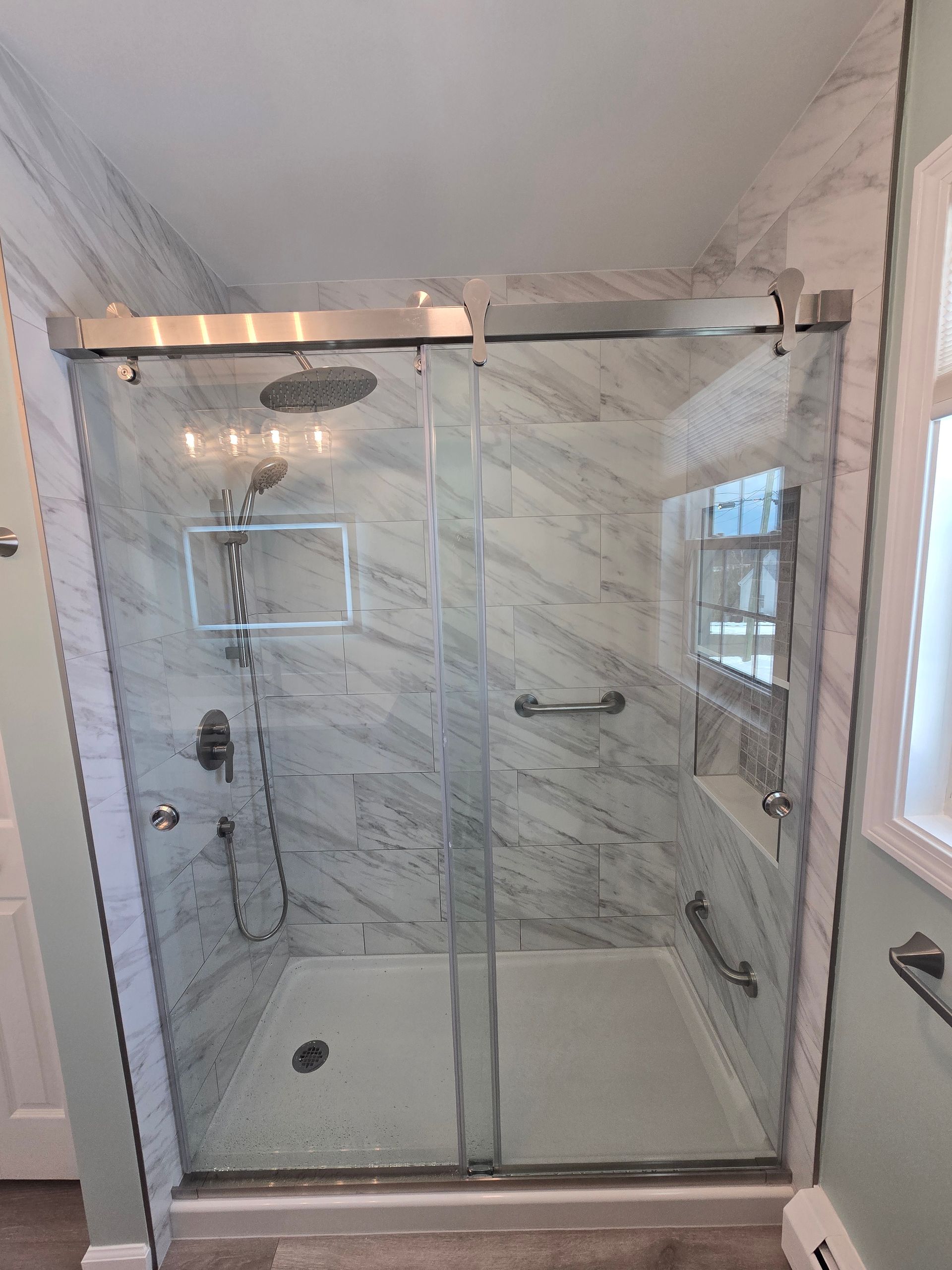 Shower stall with sliding glass doors, marble tile walls, and grab bars.