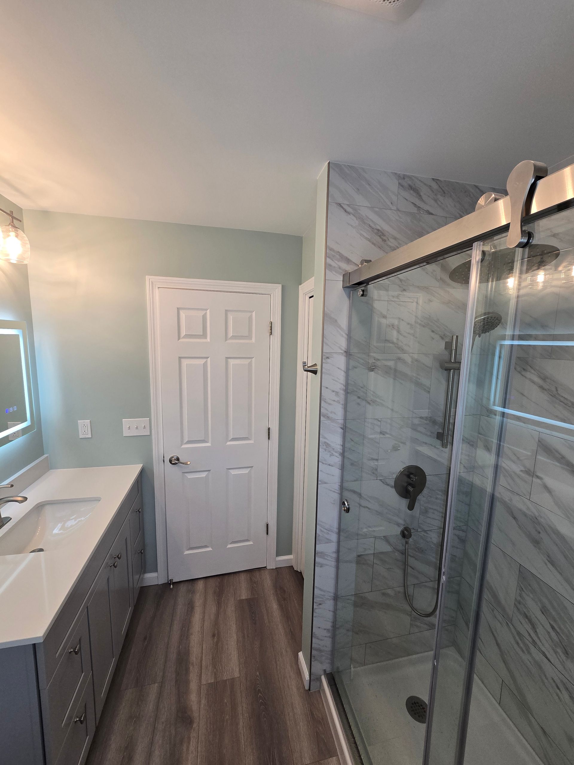Bathroom with a gray vanity, shower, and white door on light blue walls.