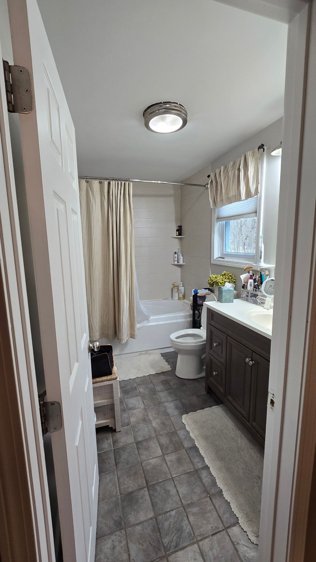 Bathroom with tiled floor, bathtub, toilet, vanity, and open doorway.