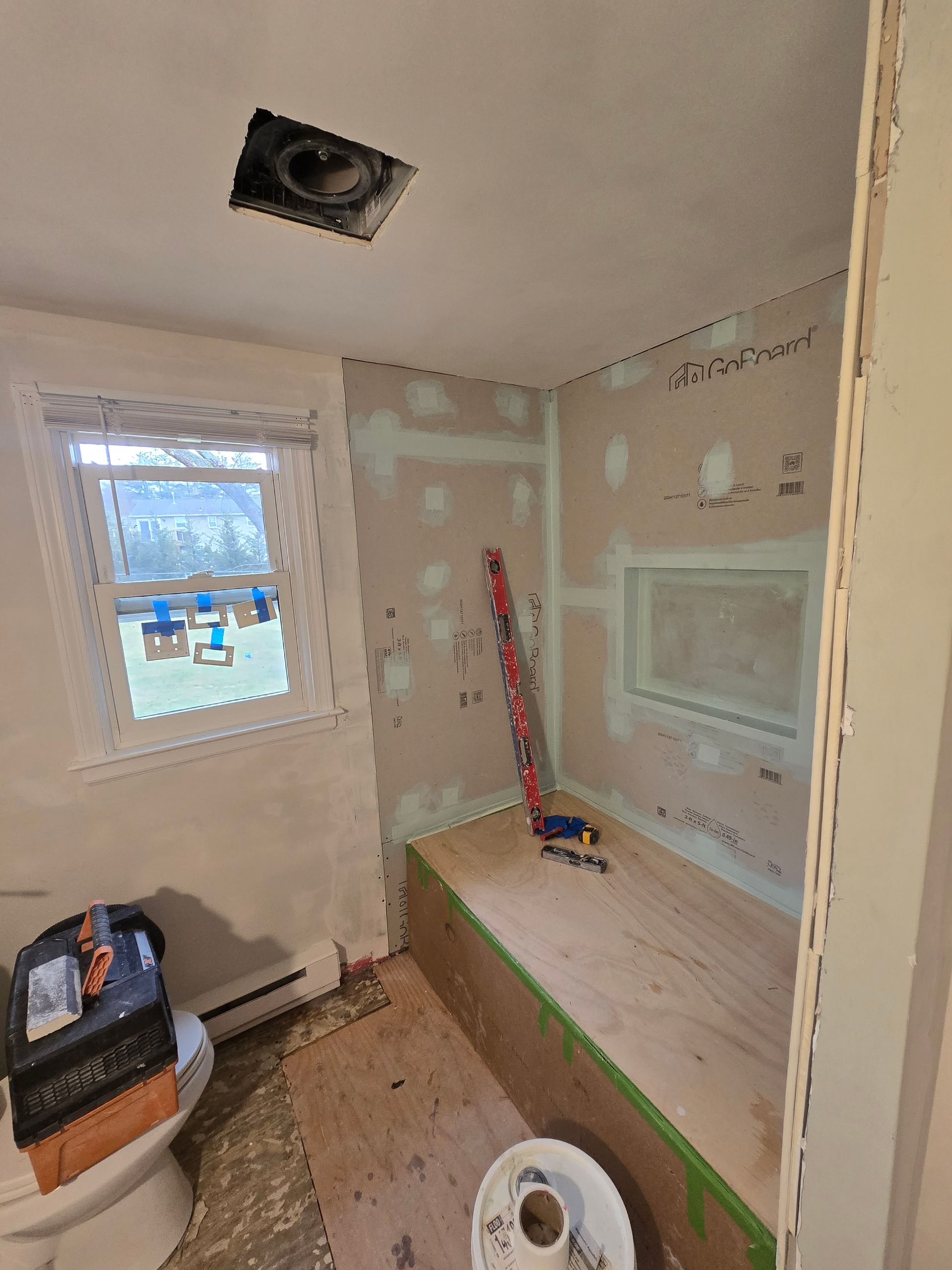 A bathroom under construction with a toilet , sink and window.