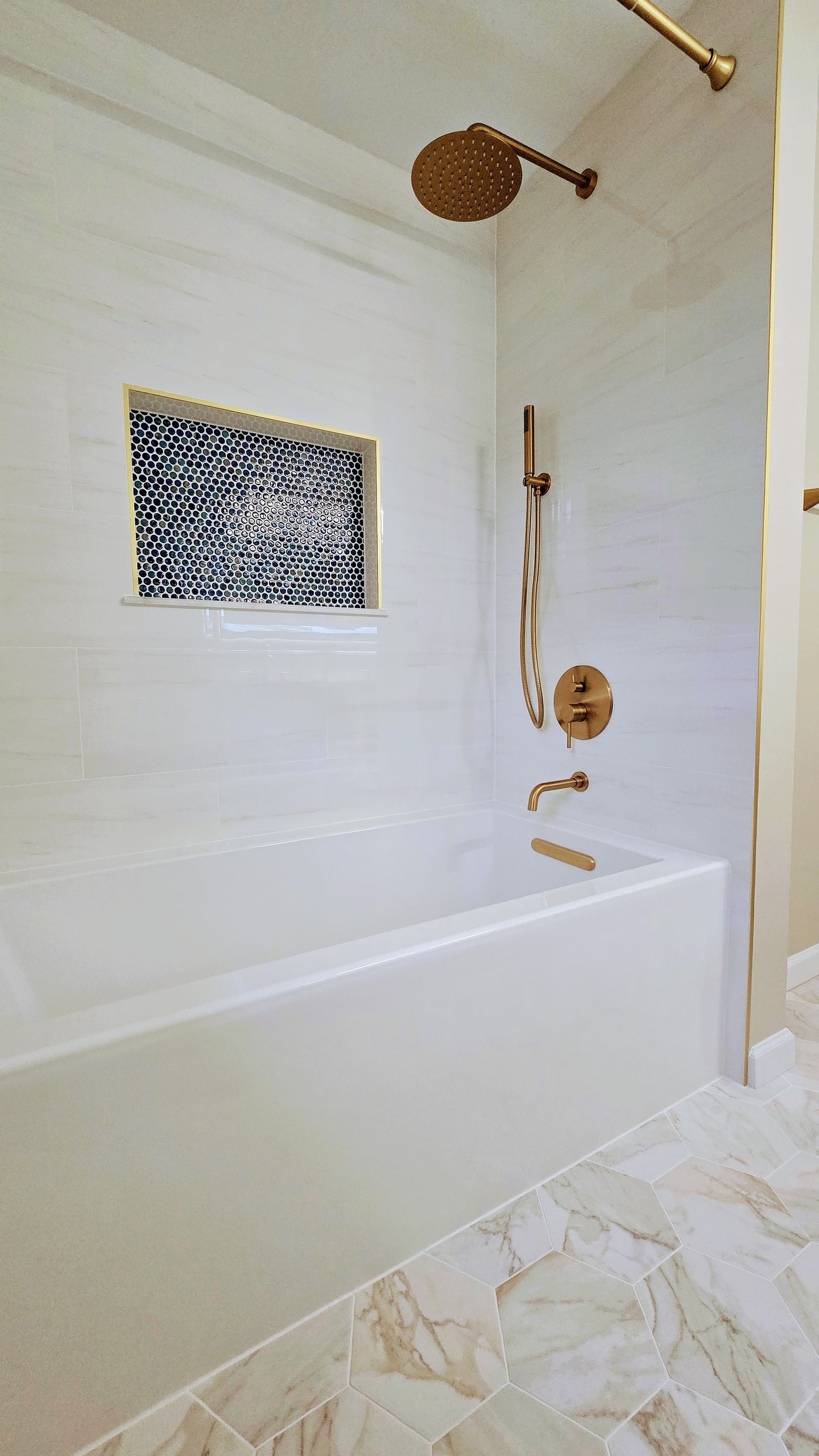 White bathroom with a tub, shower fixtures, and a mosaic accent.