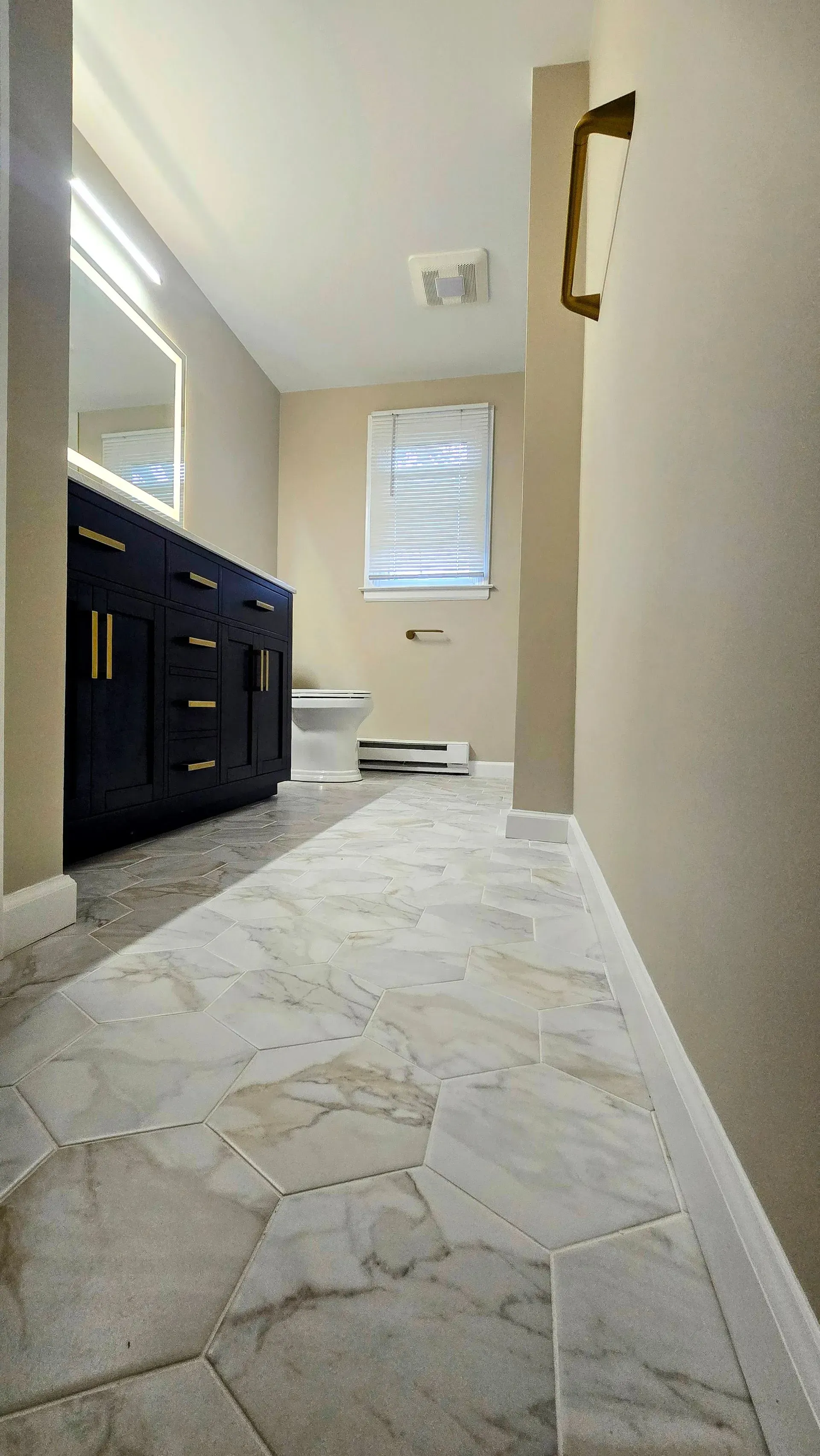 Narrow bathroom with hexagon-tiled floor, navy vanity, and window.