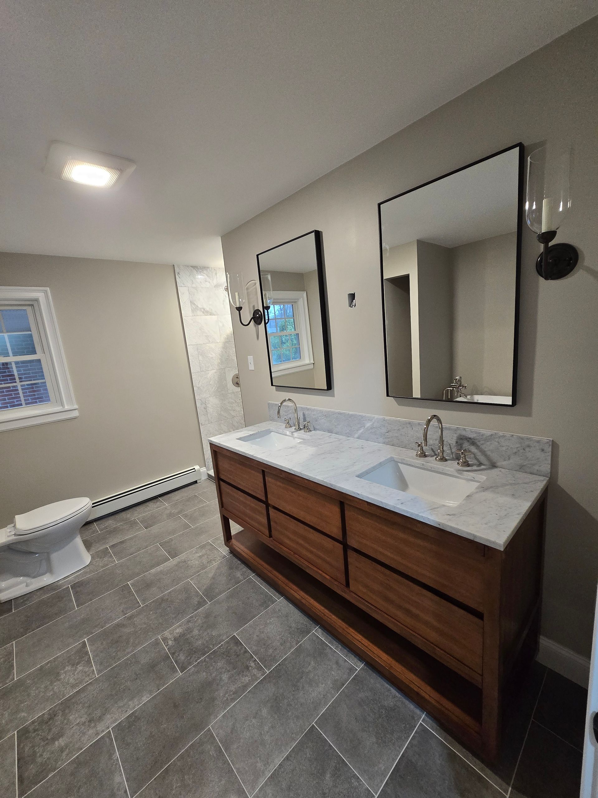 A bathroom with two sinks , two mirrors and a toilet.