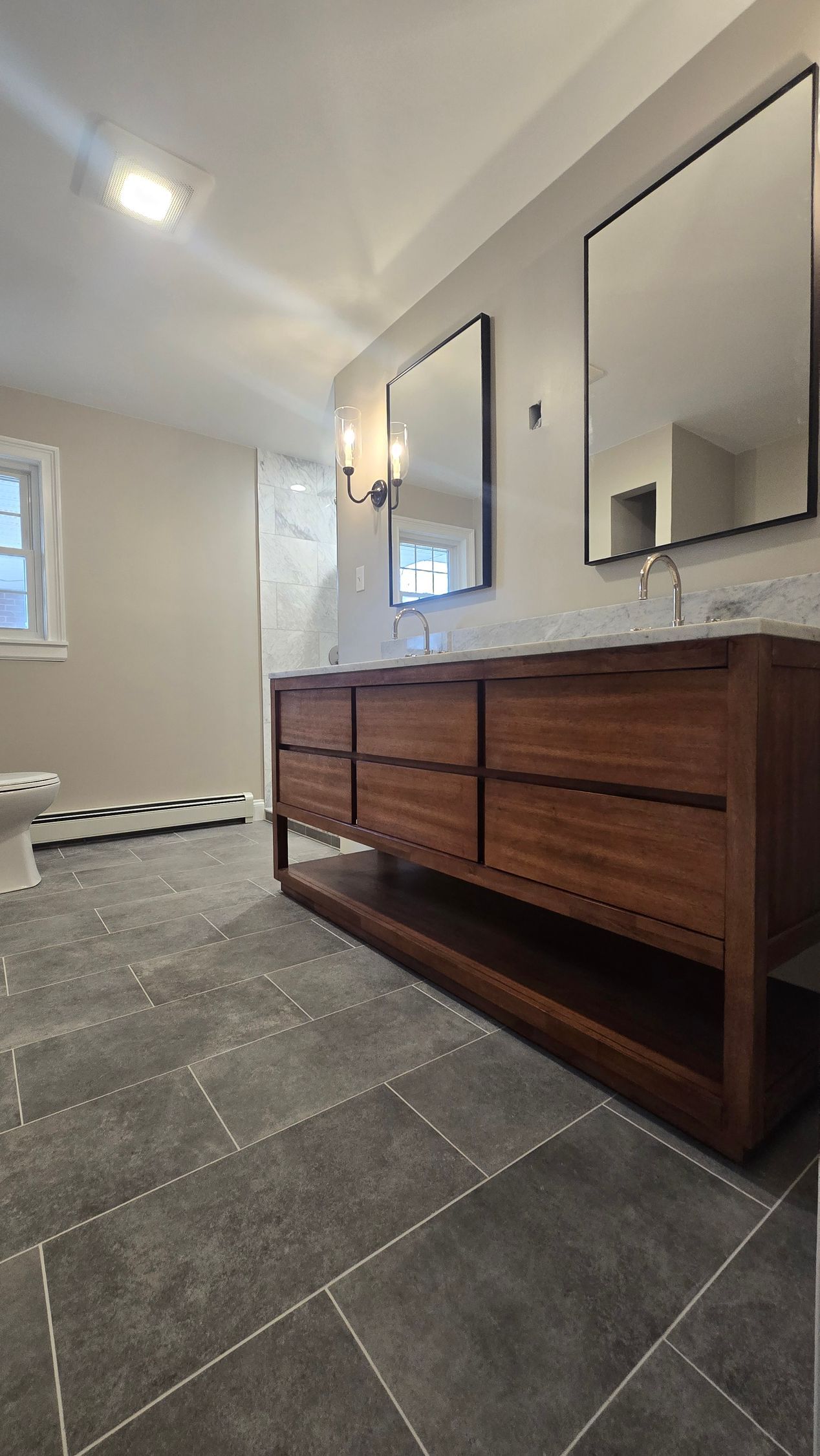 Bathroom with wood vanity, dark tile floor, and two mirrors.