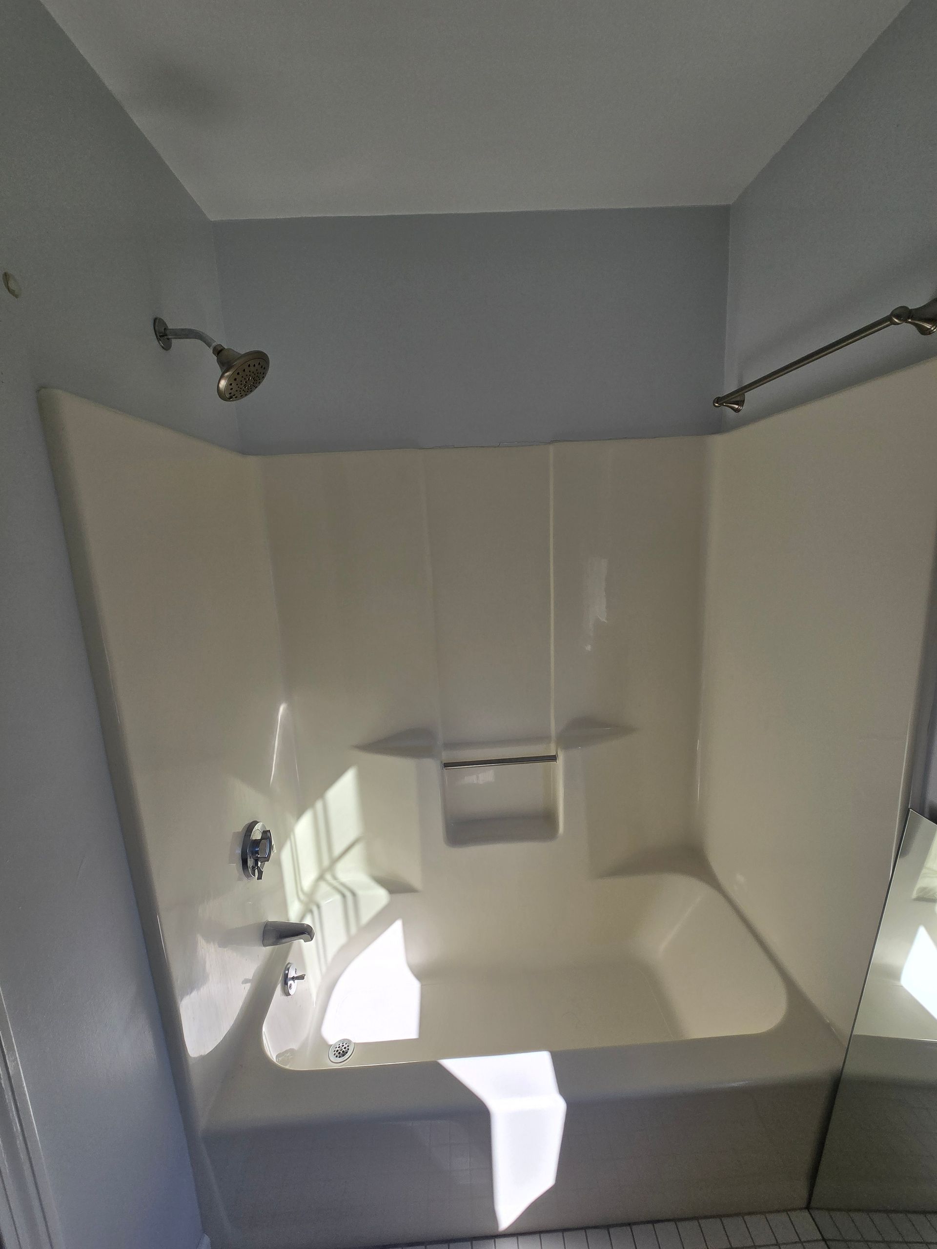 White bathtub and shower combo with chrome fixtures in a bathroom; light blue wall.