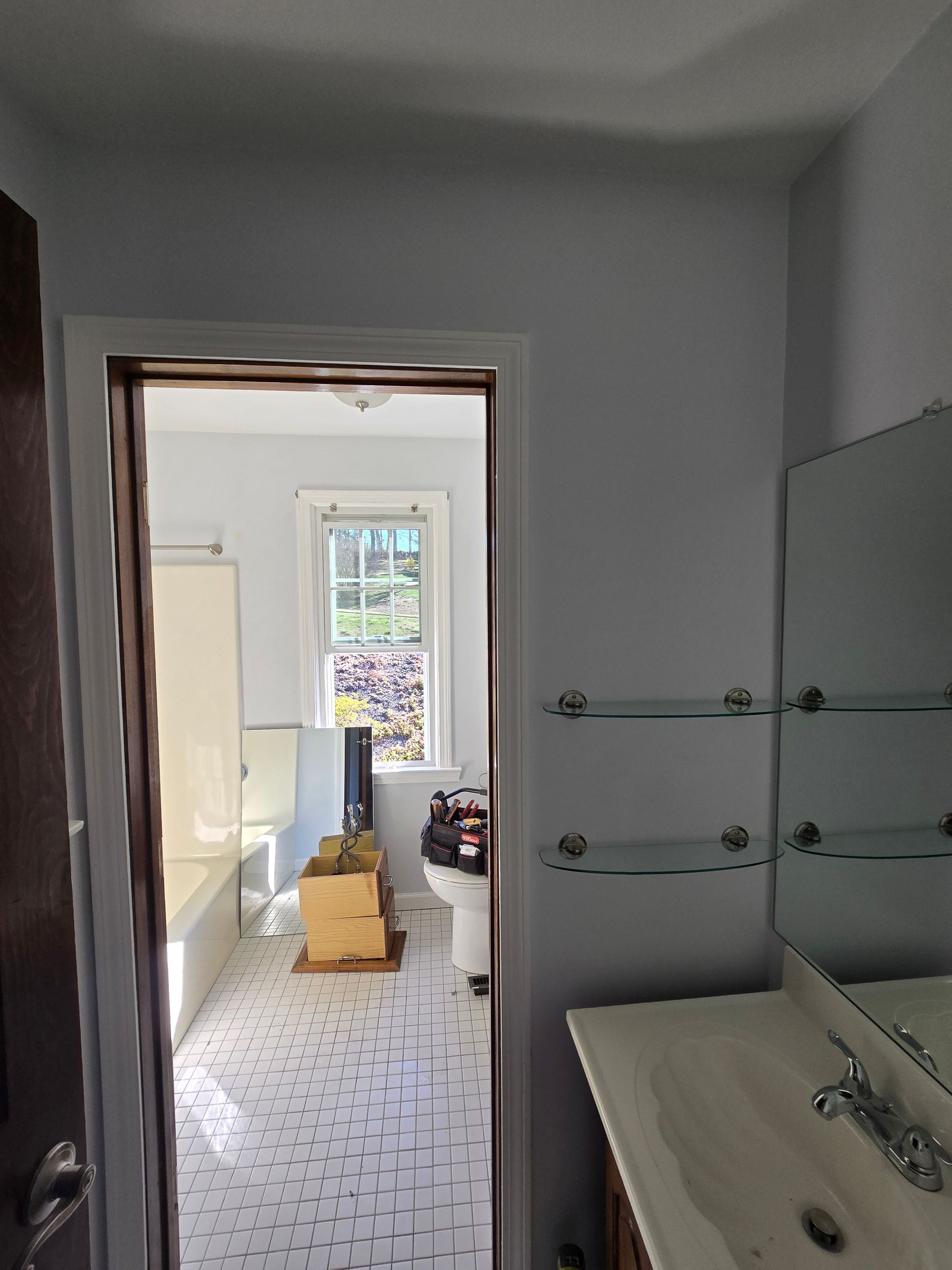 Bathroom doorway view: toilet, tub, and sink with mirror. Light blue walls, white tile floor.